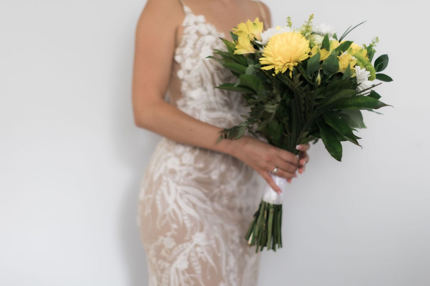 Close-up of bridal bouquet with yellow gerbera daisies against white lace wedding dress.