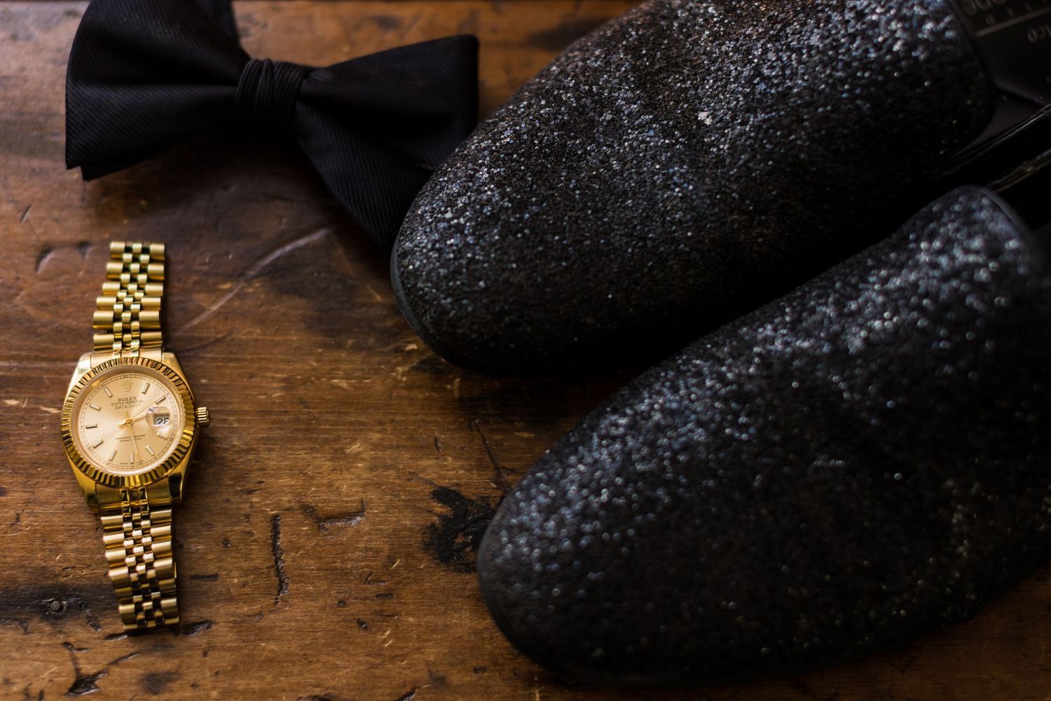 Gold watch and black bow tie laid out on wooden surface as wedding accessories.