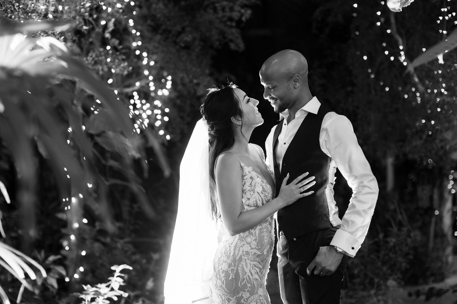 Romantic black and white portrait of newlyweds embracing under twinkling lights.
