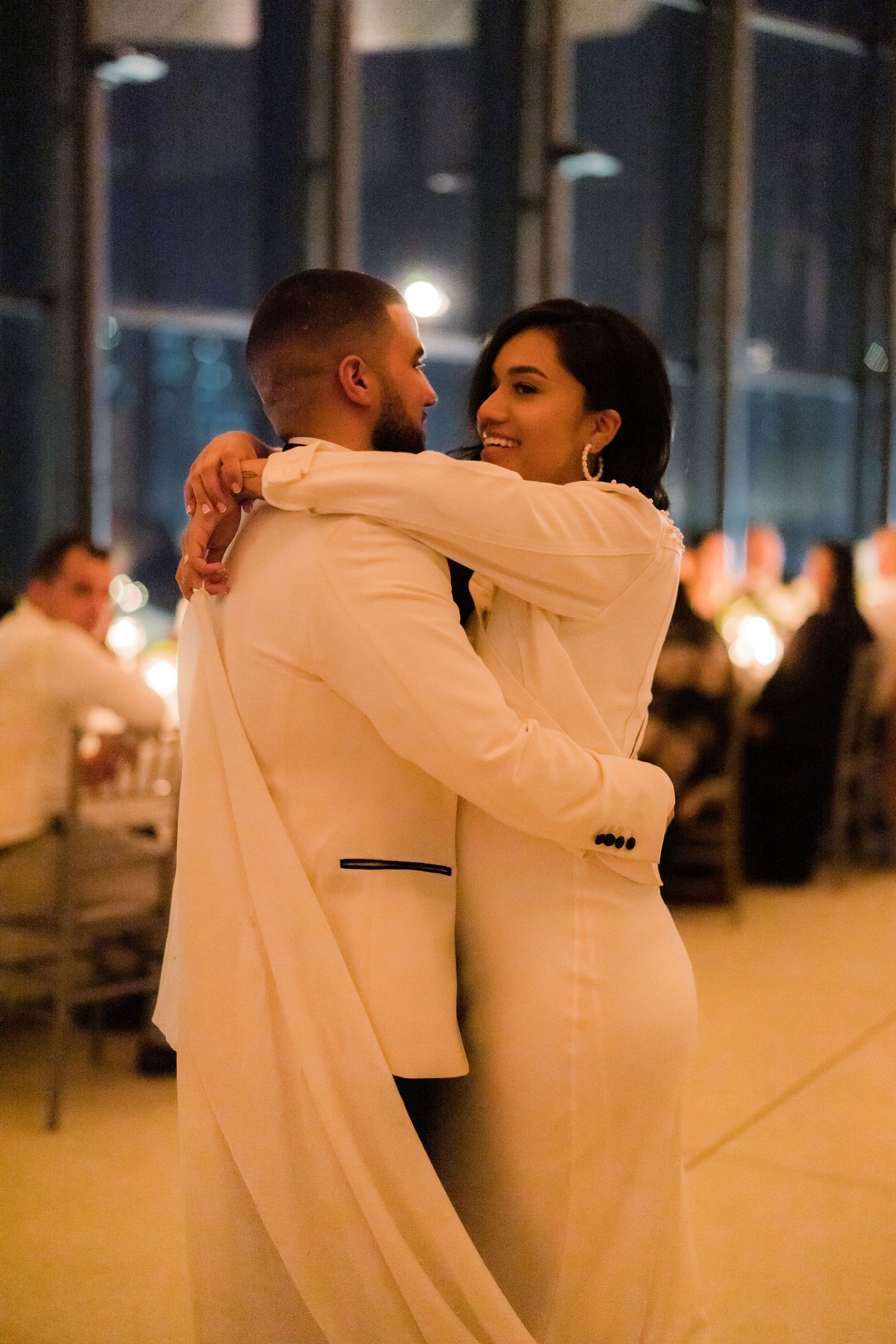 A couple in white formal attire share an intimate dance at their wedding reception.