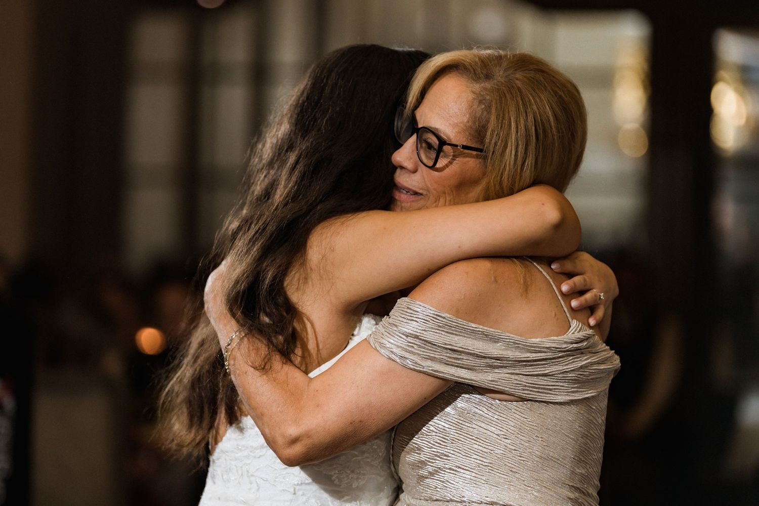 Two people share a warm embrace during an indoor wedding celebration.