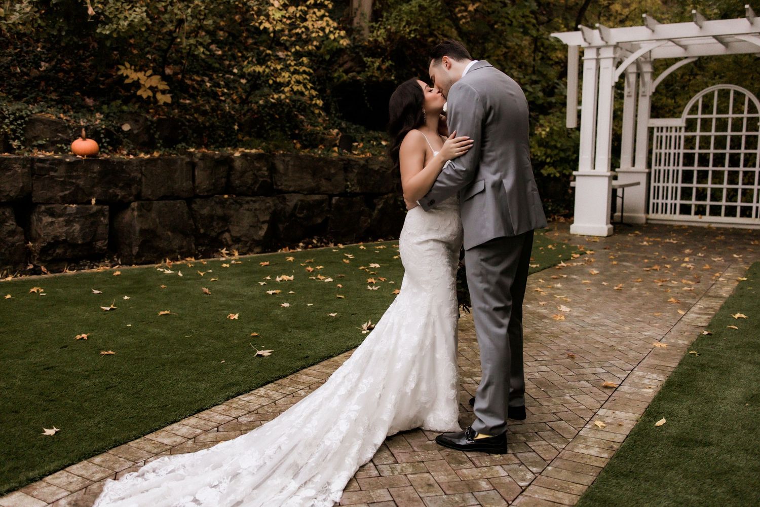 Couple shares romantic kiss under garden arbor during wedding celebration.