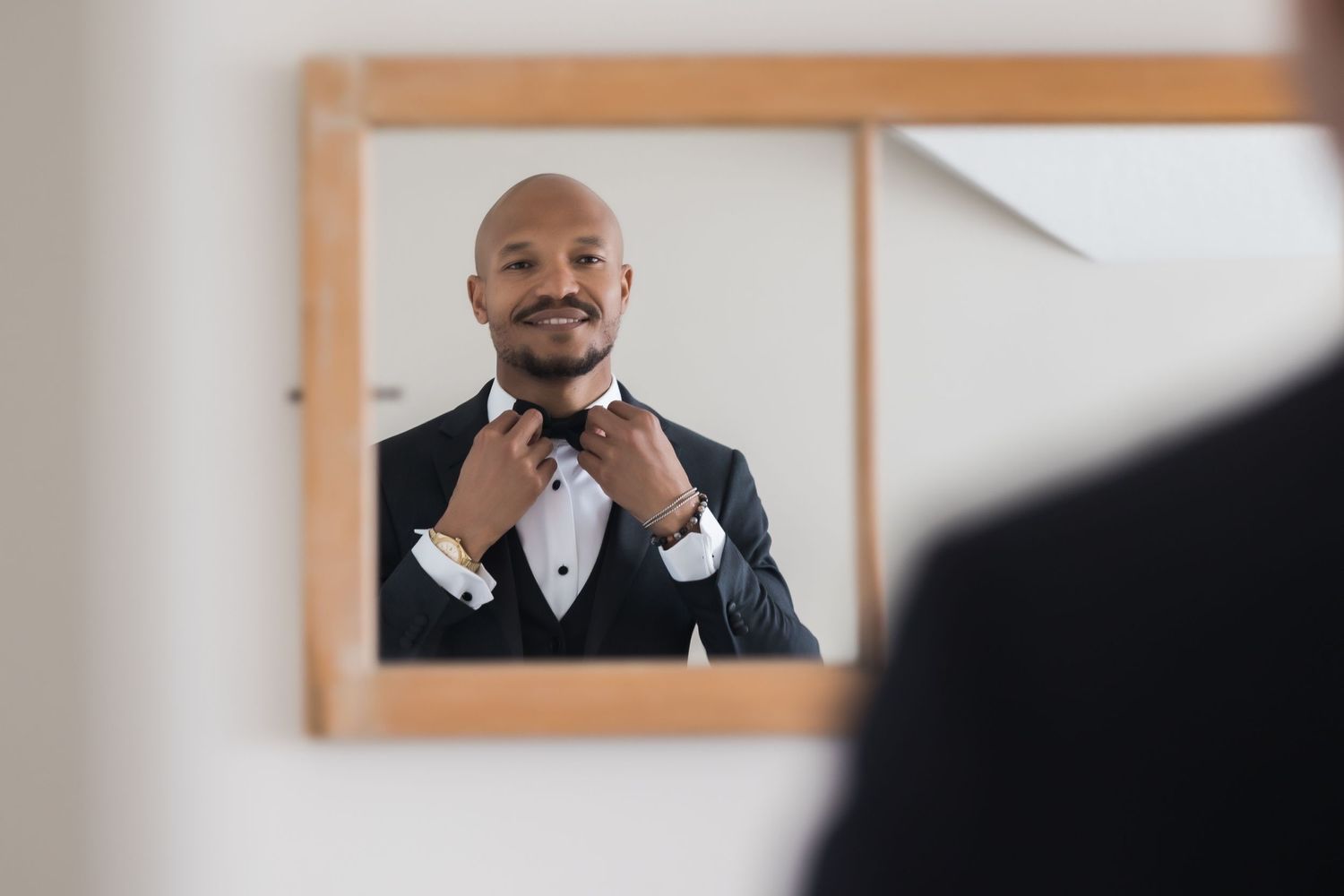 Mirror reflection shows person adjusting bow tie while getting ready in formal wear.