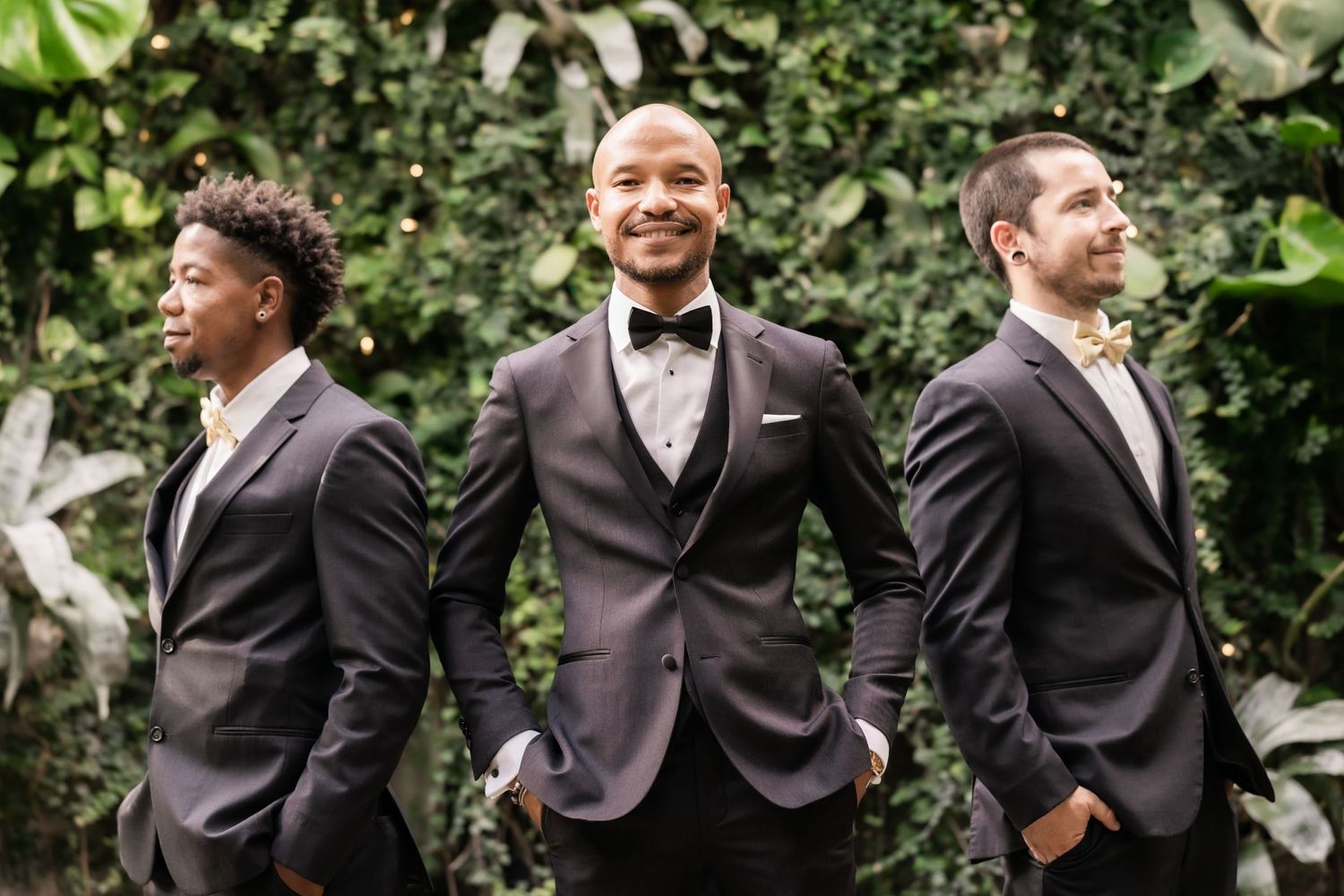 Groomsmen in dark suits pose together against garden backdrop.