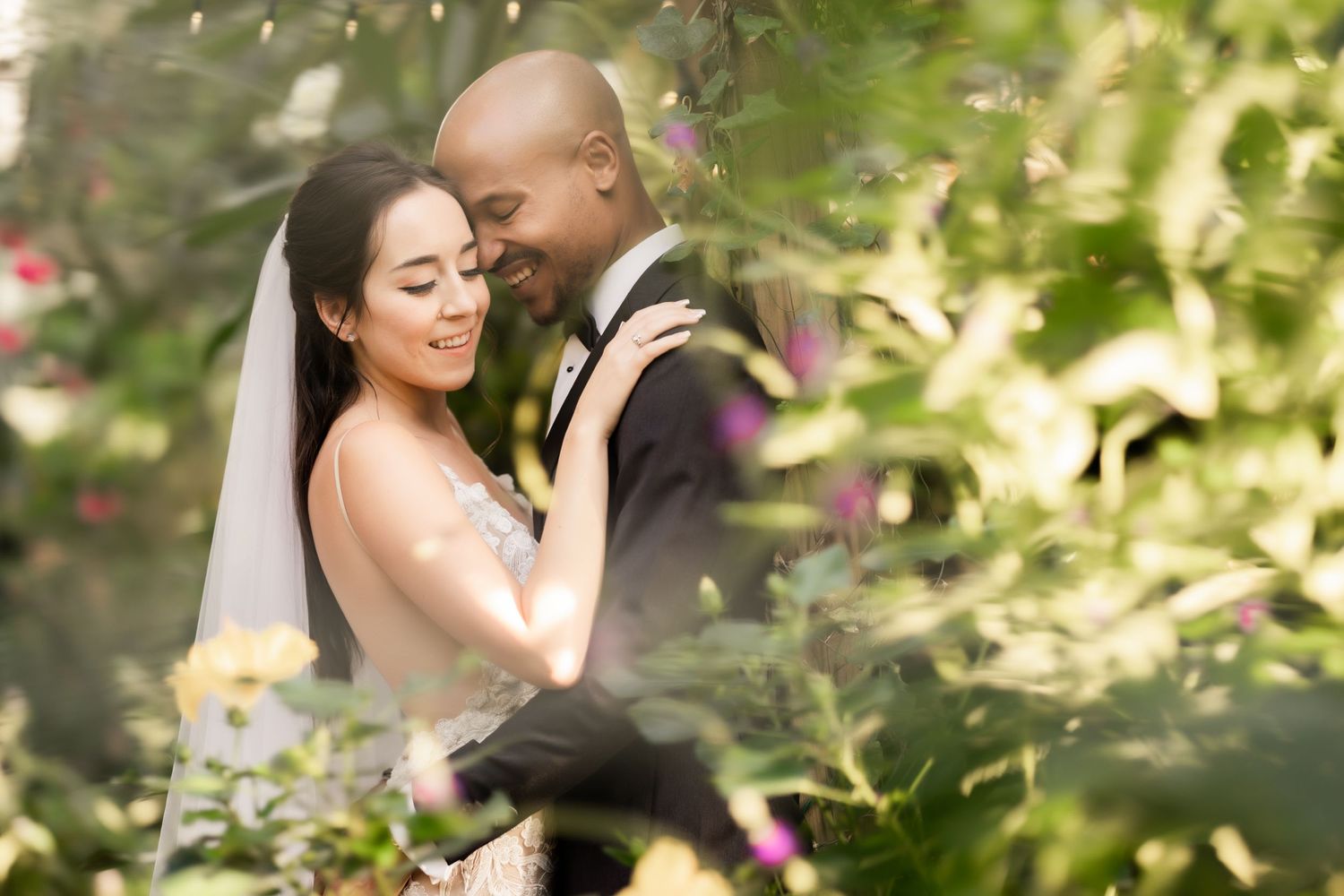Romantic wedding portrait of couple embracing in a sun-dappled garden setting.