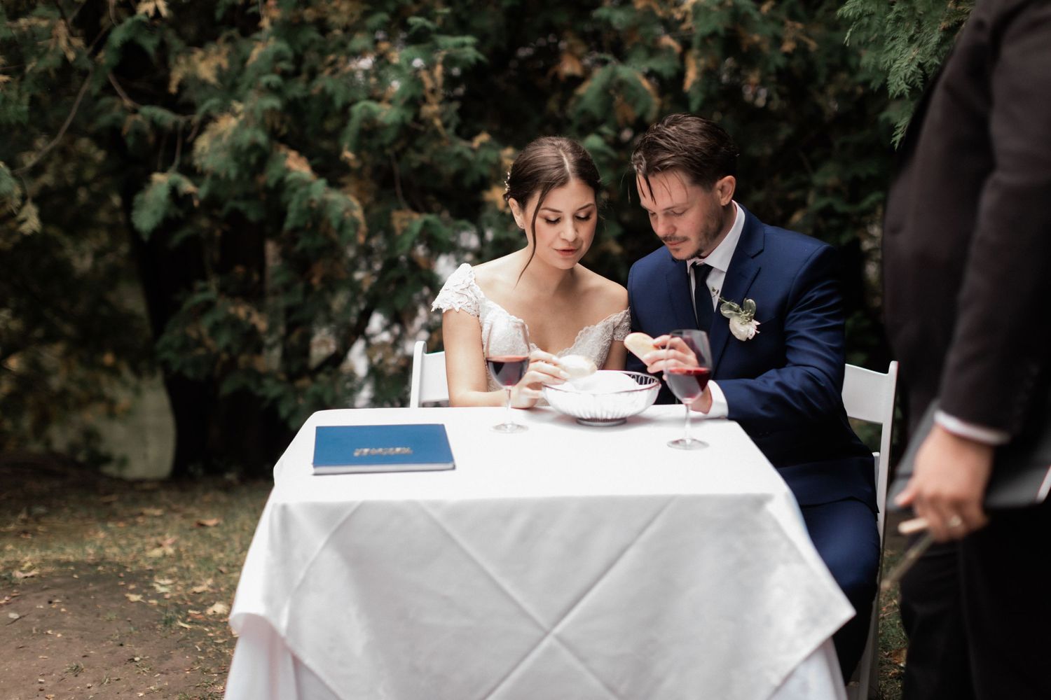 Couple seated at white-clothed table during their wedding reception in a garden setting.