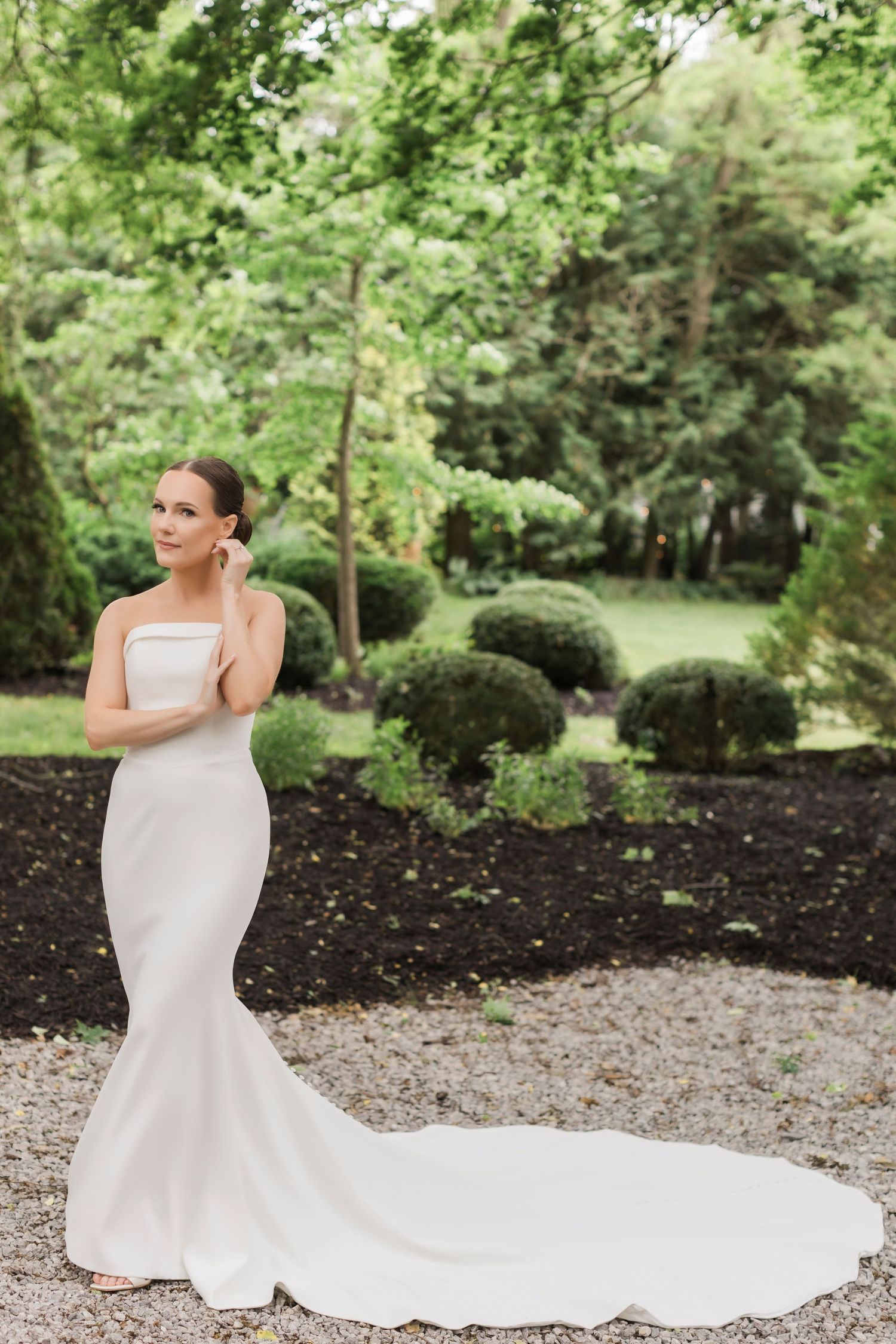 Classic fitted wedding gown with dramatic train shown against manicured garden landscape.