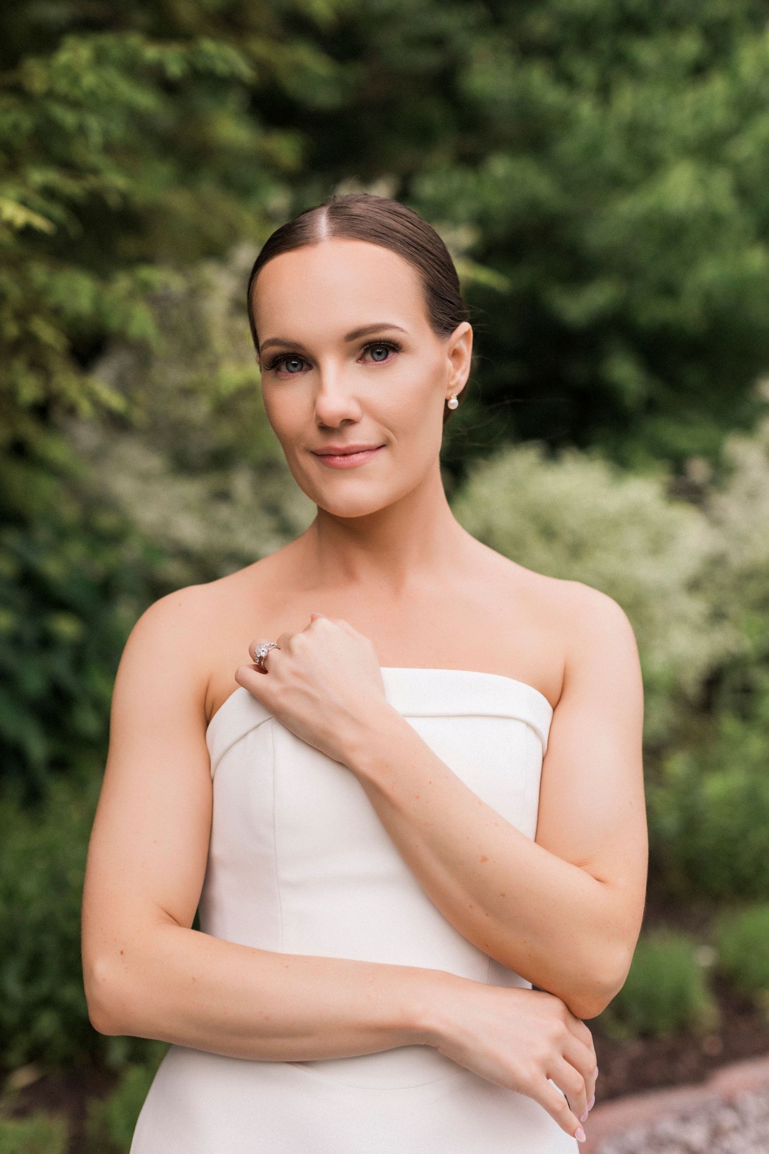 A bride poses elegantly in her strapless wedding gown against a natural green backdrop.