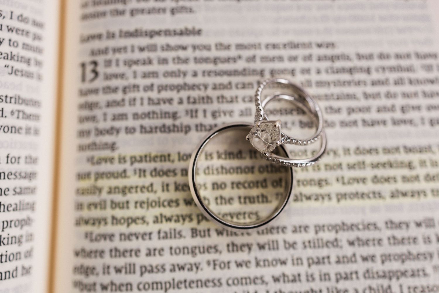 Wedding rings rest on an open Bible page displaying text about prophecy and spiritual gifts.