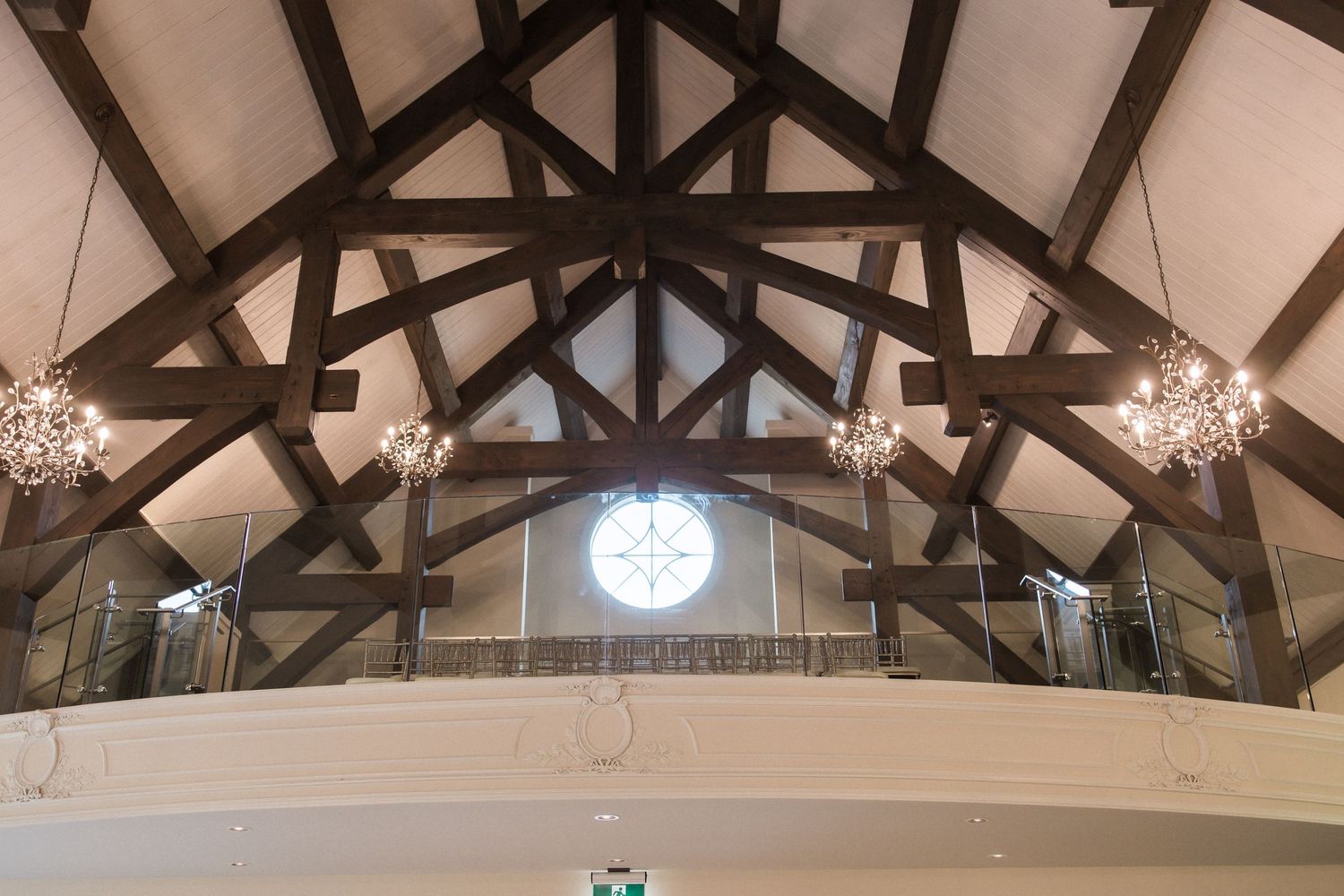 Cathedral ceiling with dark wooden beams and crystal chandeliers in wedding venue.