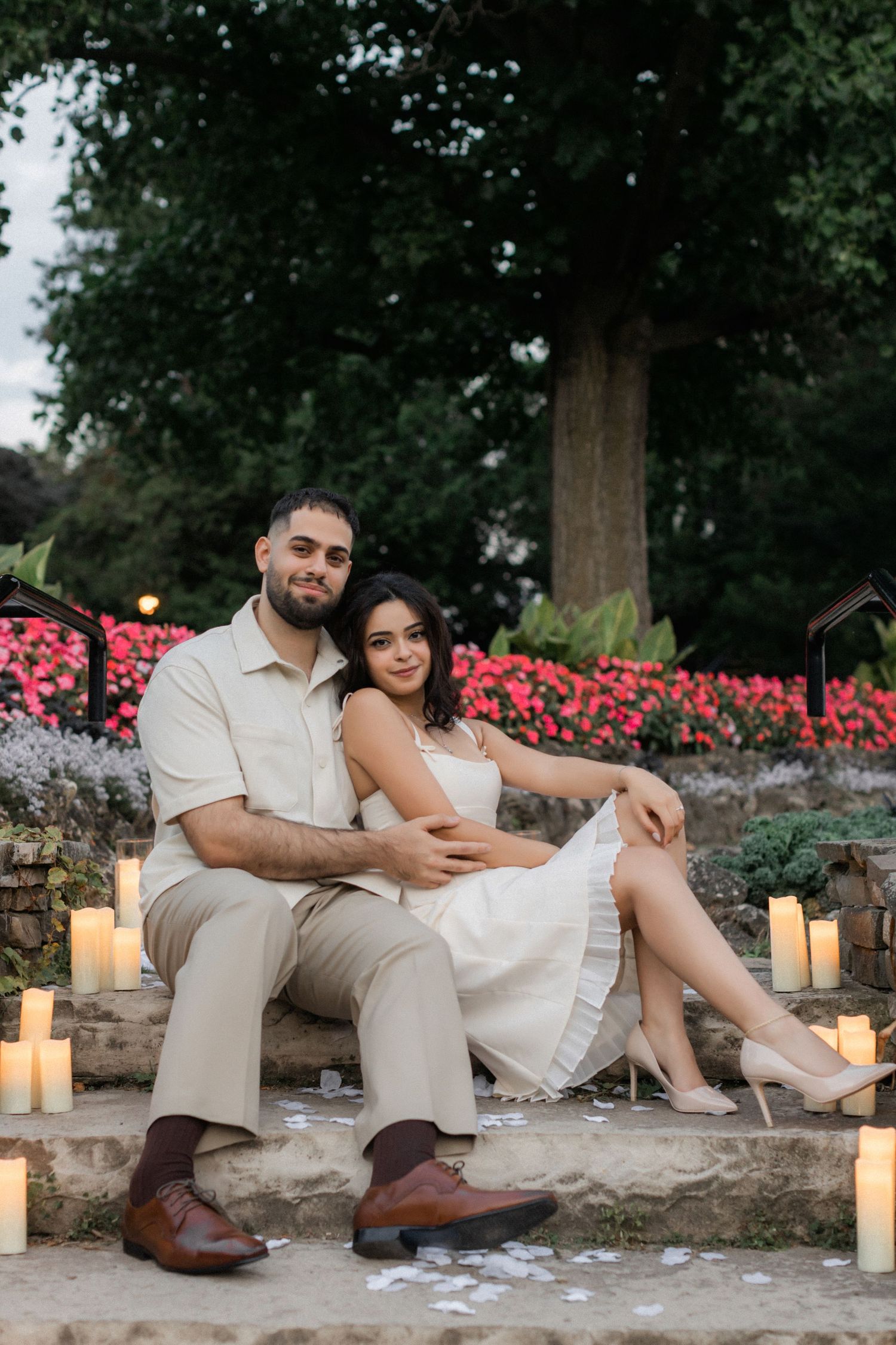 A romantic evening portrait with glowing candles and pink flowers in a garden setting.