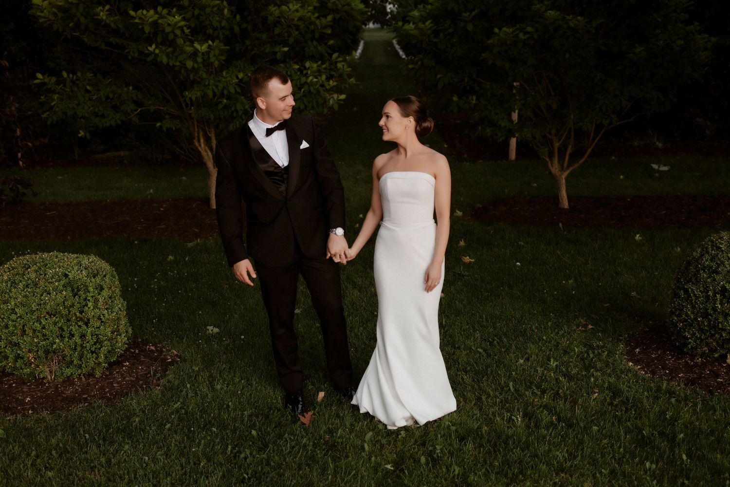 Elegant wedding couple sharing a romantic moment while walking through a lush garden at sunset.