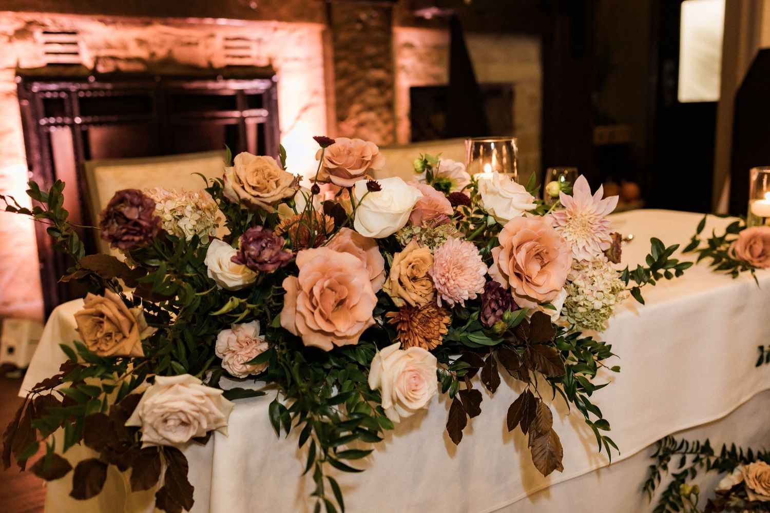 Luxurious floral arrangement with blush roses and greenery on wedding reception table.