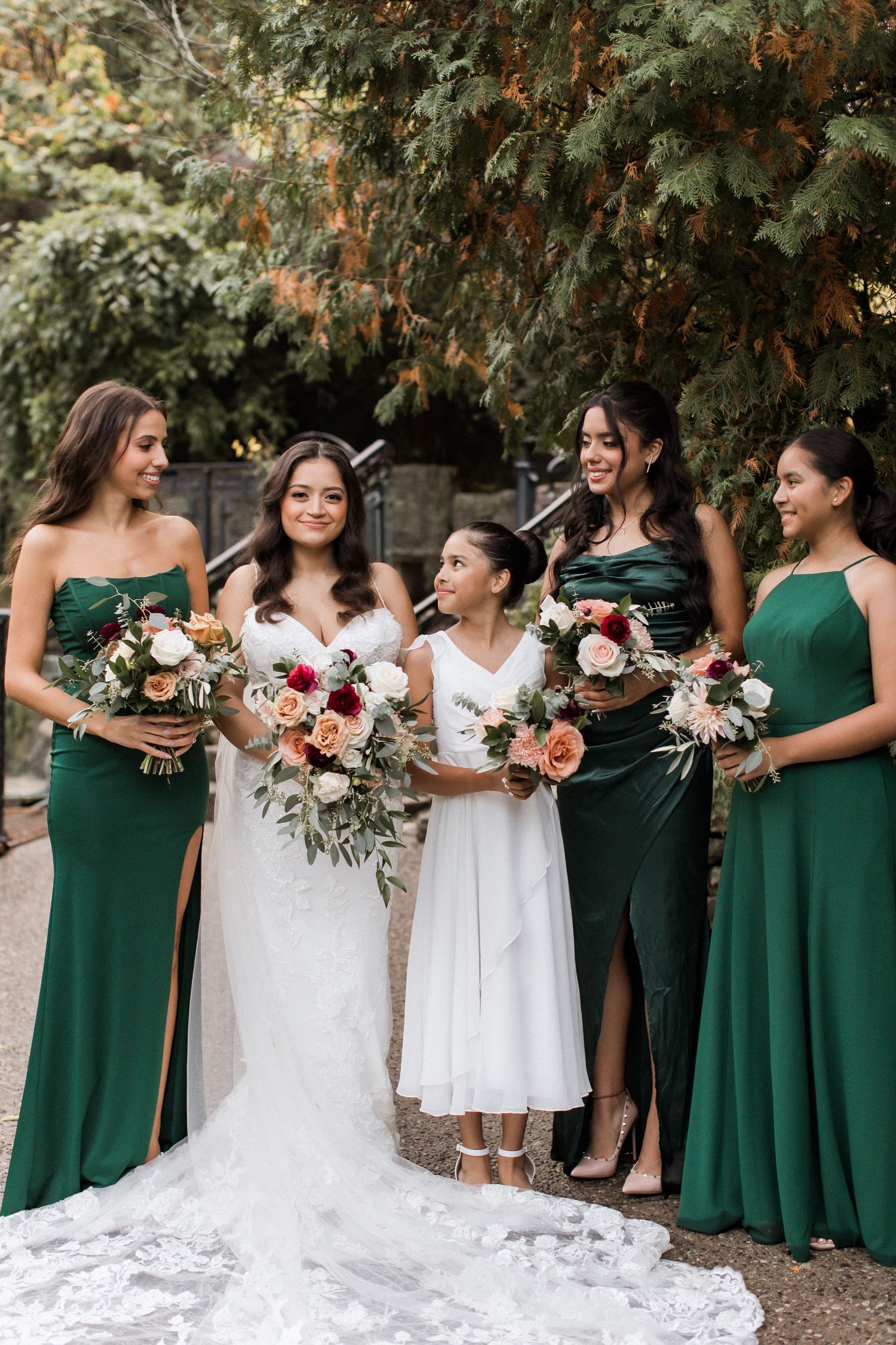 Bridal party in emerald gowns share a candid moment while holding lush floral bouquets.