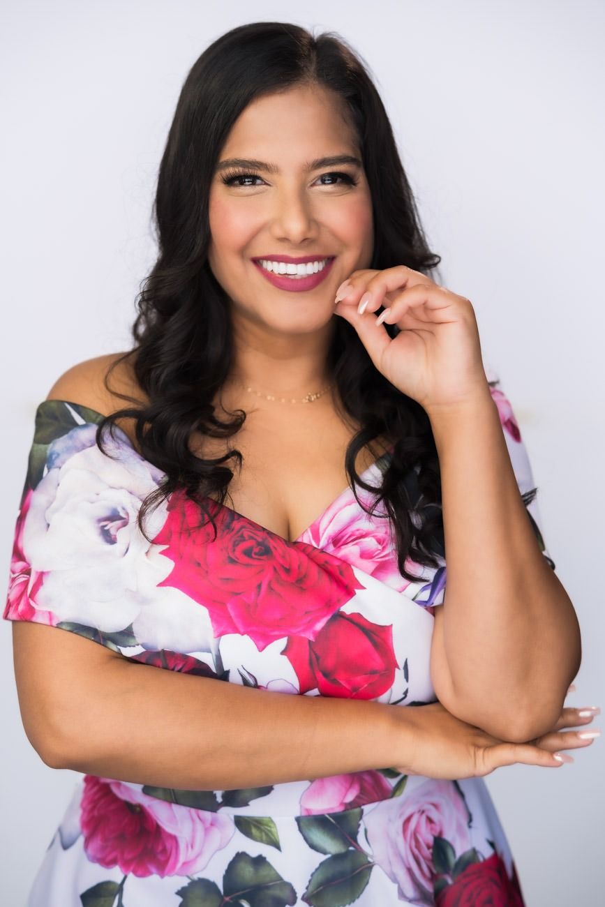 Portrait of a woman in a floral dress smiling against a white background.