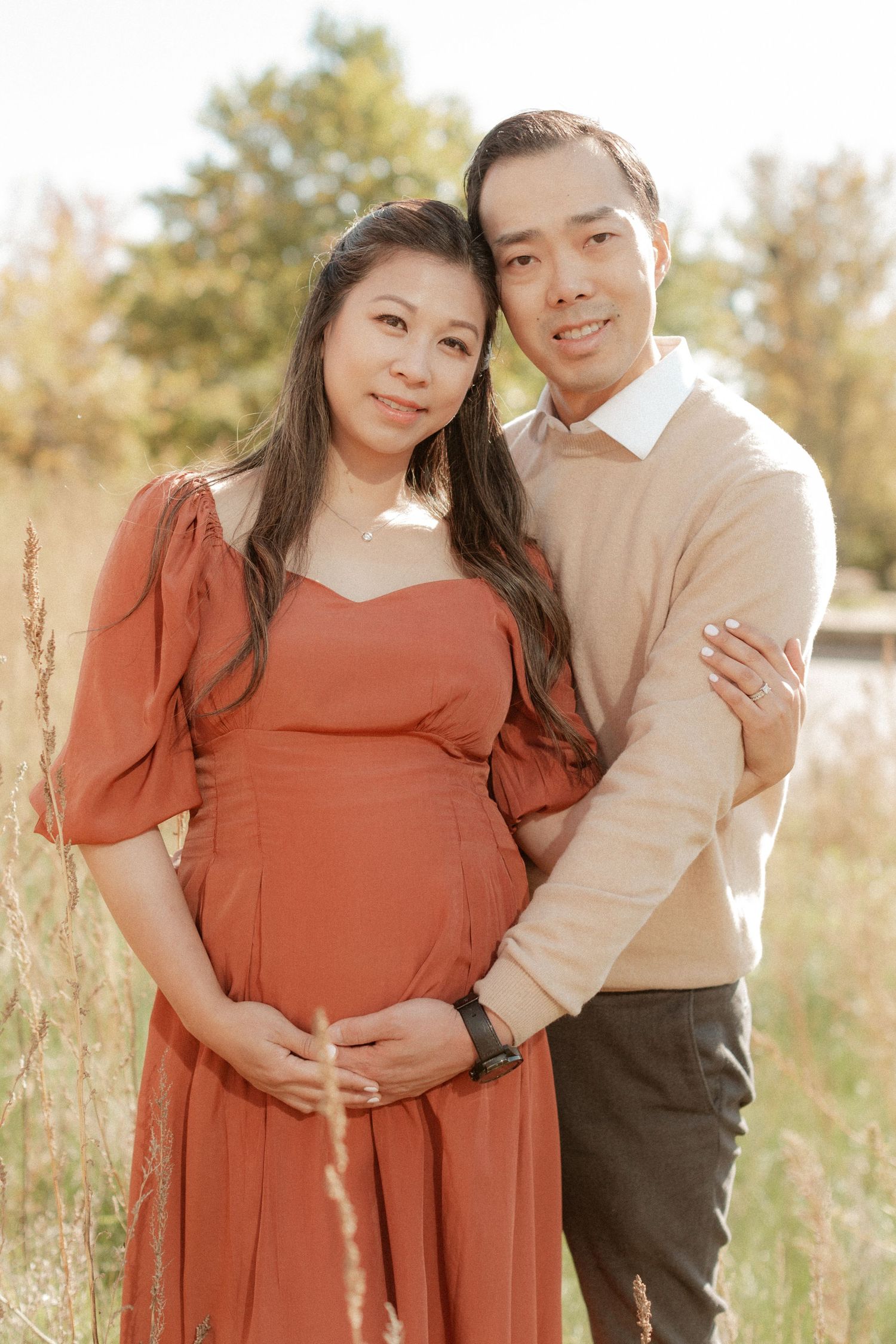 A couple poses together for a maternity photo in a golden field during sunset.