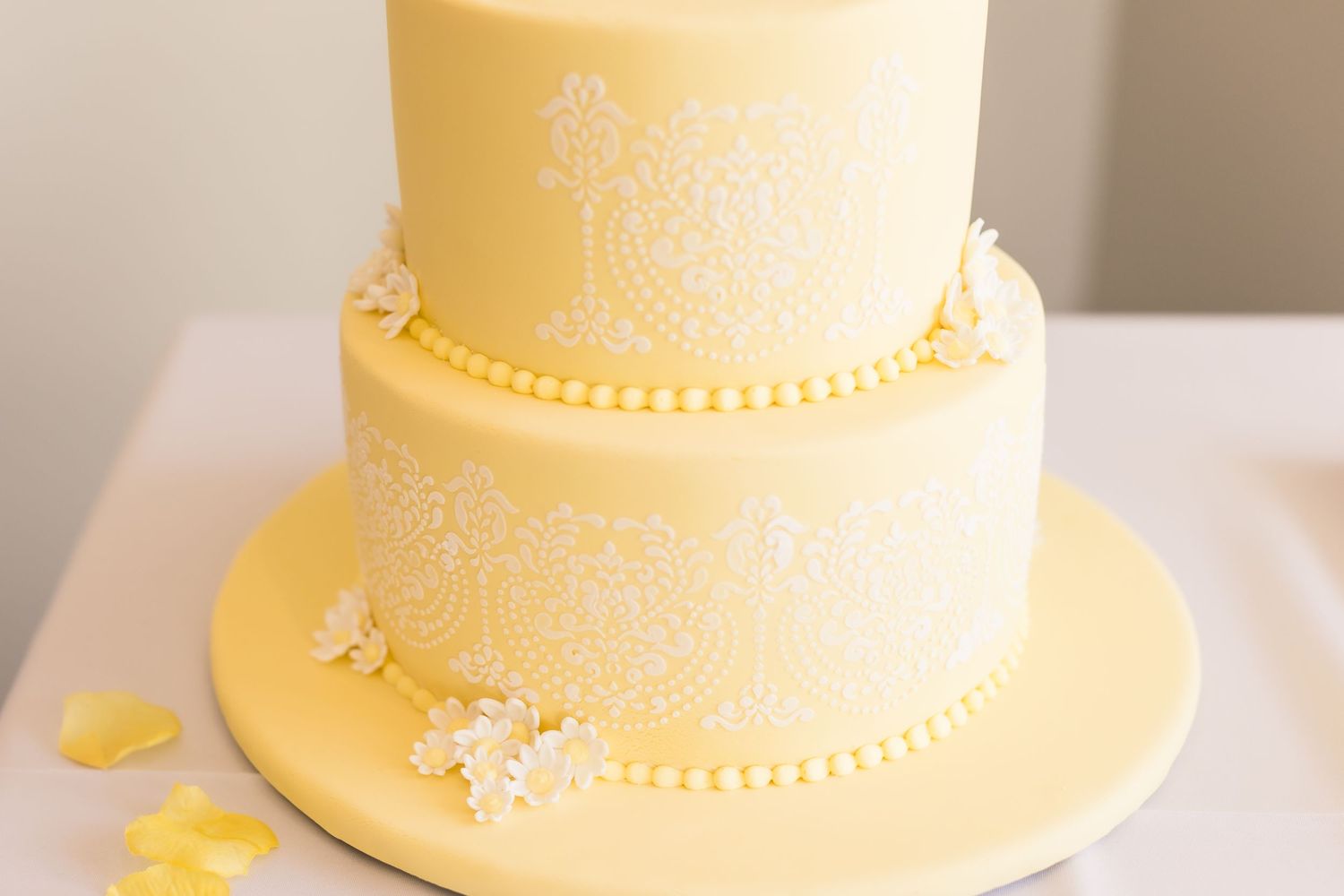 Elegant butter yellow wedding cake with white piped details and small bow accents.