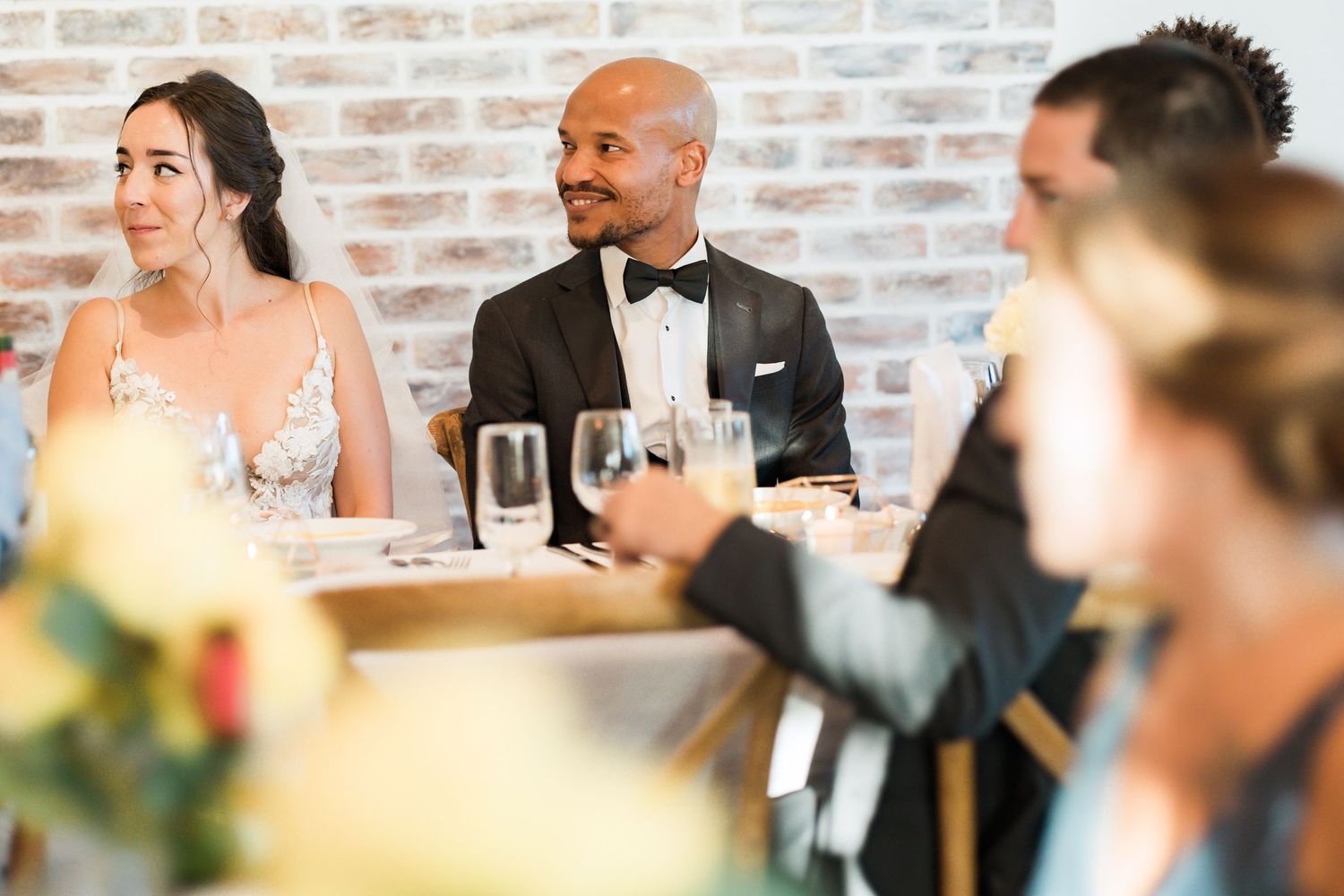 Guests and newlyweds seated at an elegant wedding reception with exposed brick walls.