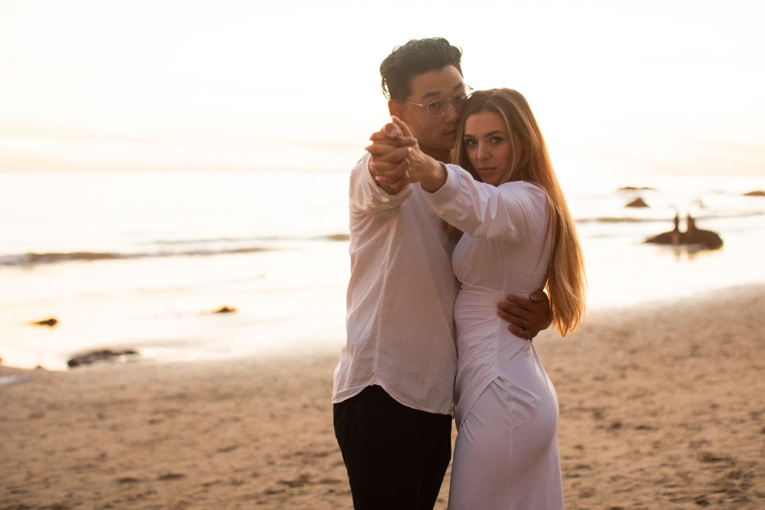 Couple dancing together on a sandy beach during golden hour.