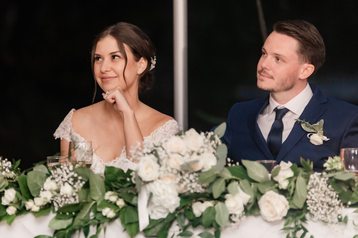 Newlyweds at wedding reception table adorned with elegant white floral arrangements and greenery.