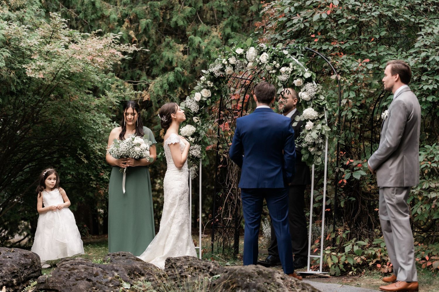 Outdoor wedding ceremony in progress with floral arch and wedding party in attendance.