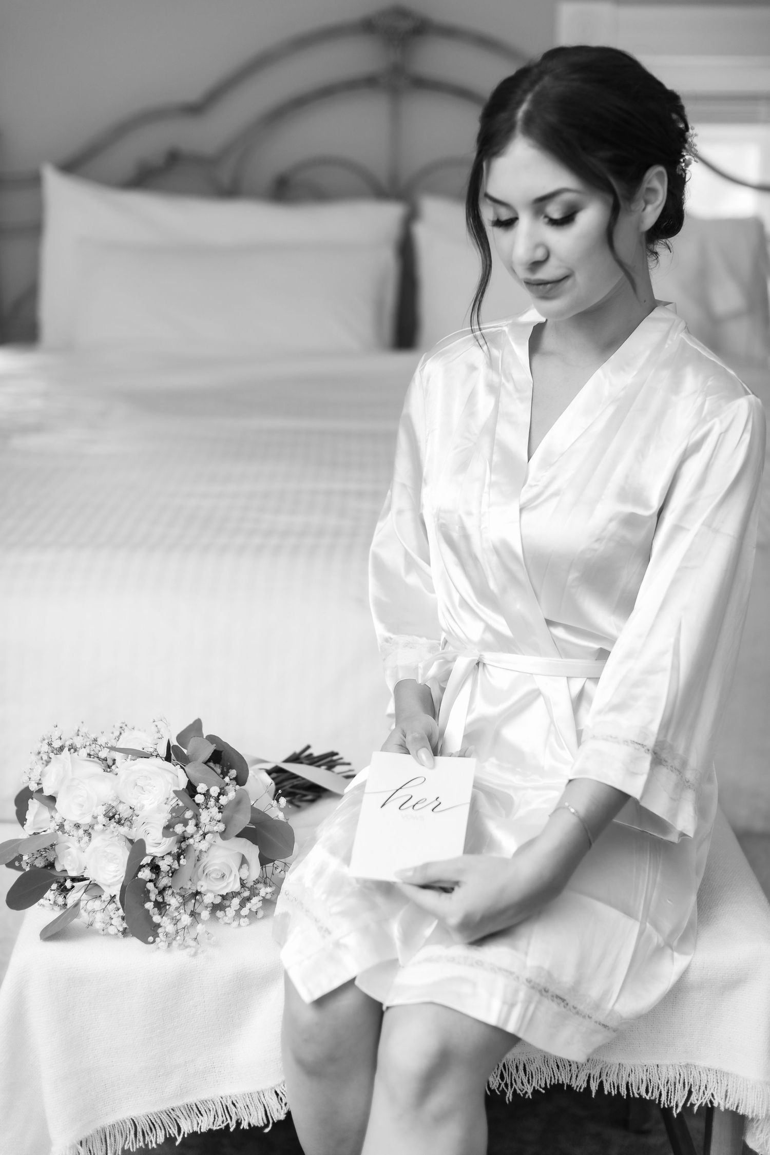 Black and white photo of bridal preparation with silk robe and wedding details.