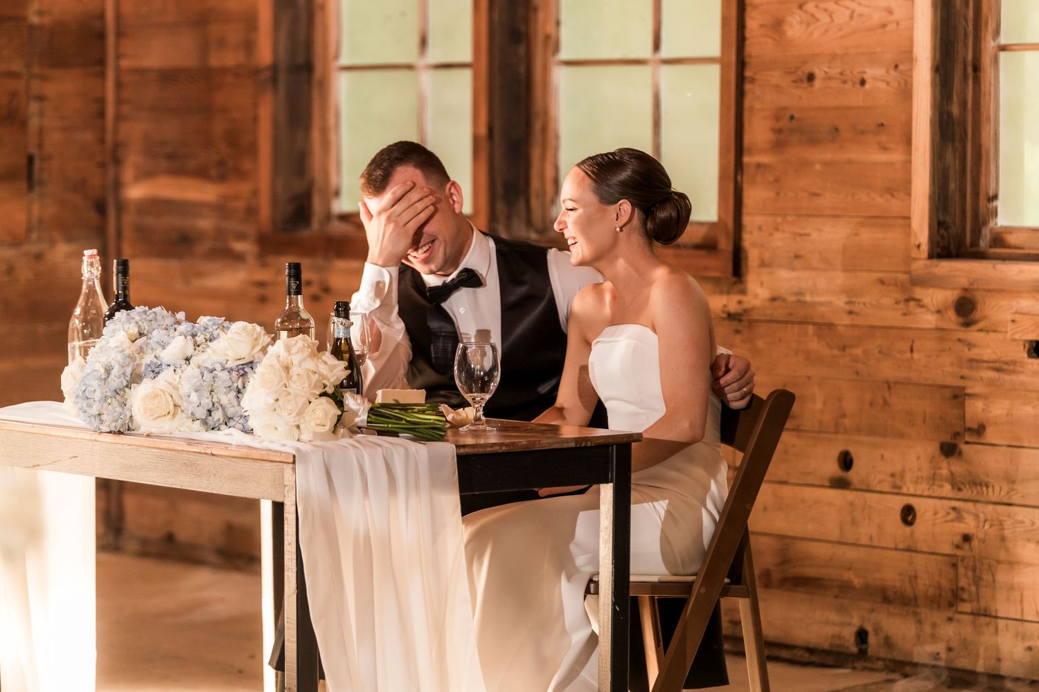 A couple shares a candid emotional moment at their rustic barn wedding reception table.