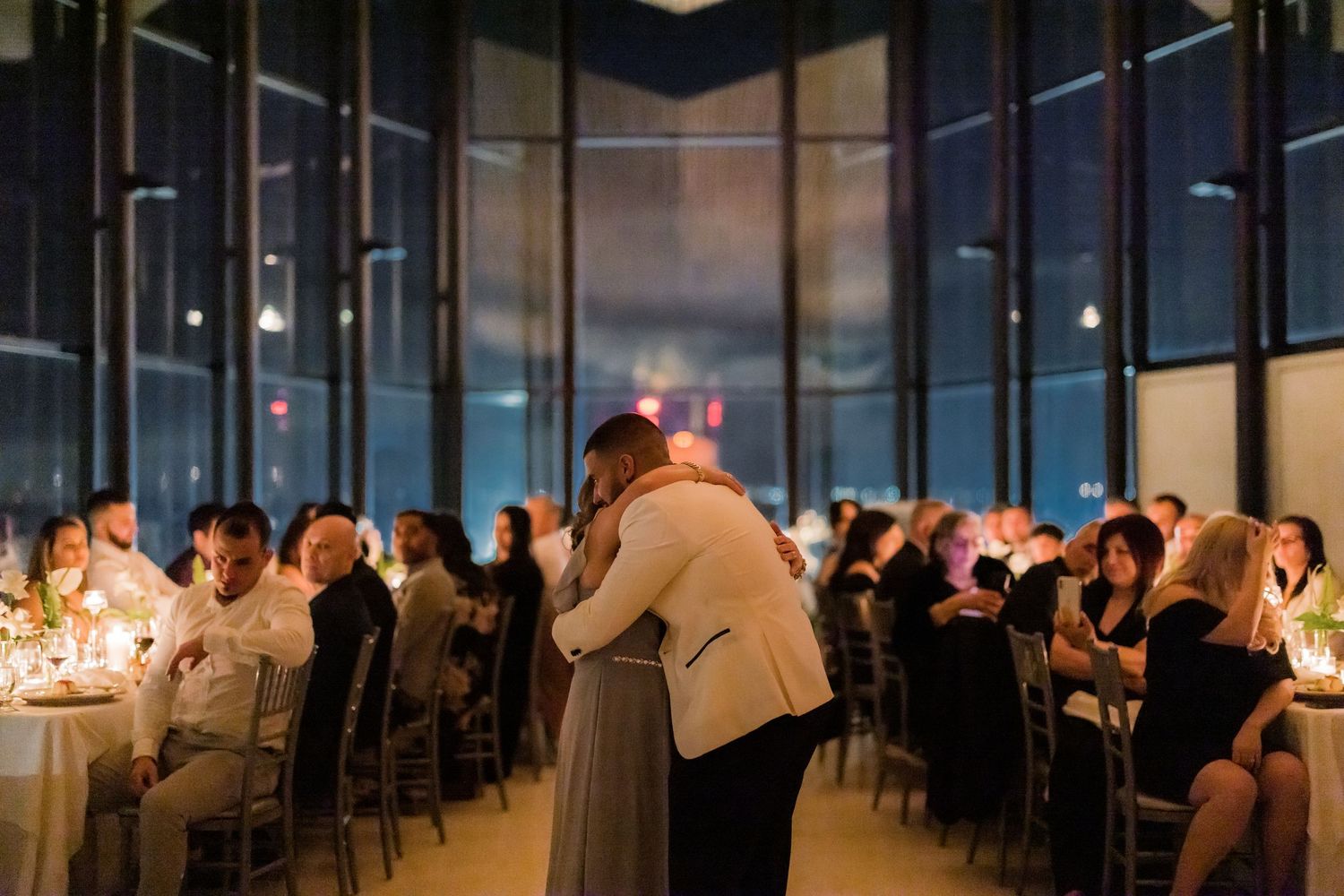 A couple dancing in an intimate moment surrounded by candlelit tables and guests at a wedding reception.
