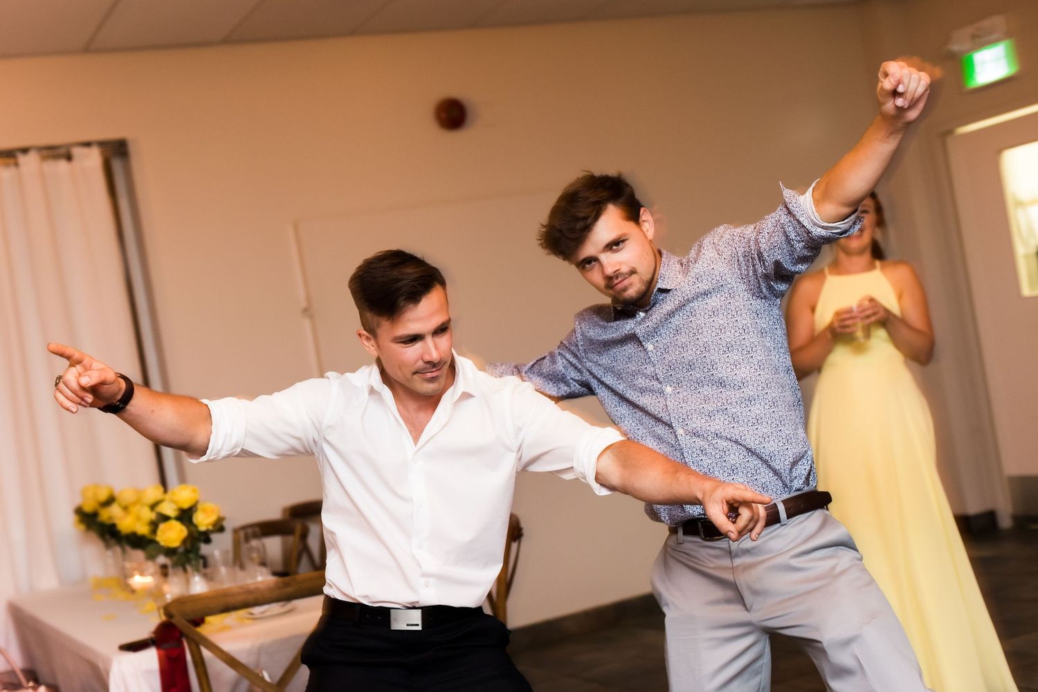 Two party guests strike enthusiastic dance poses at a festive indoor celebration.