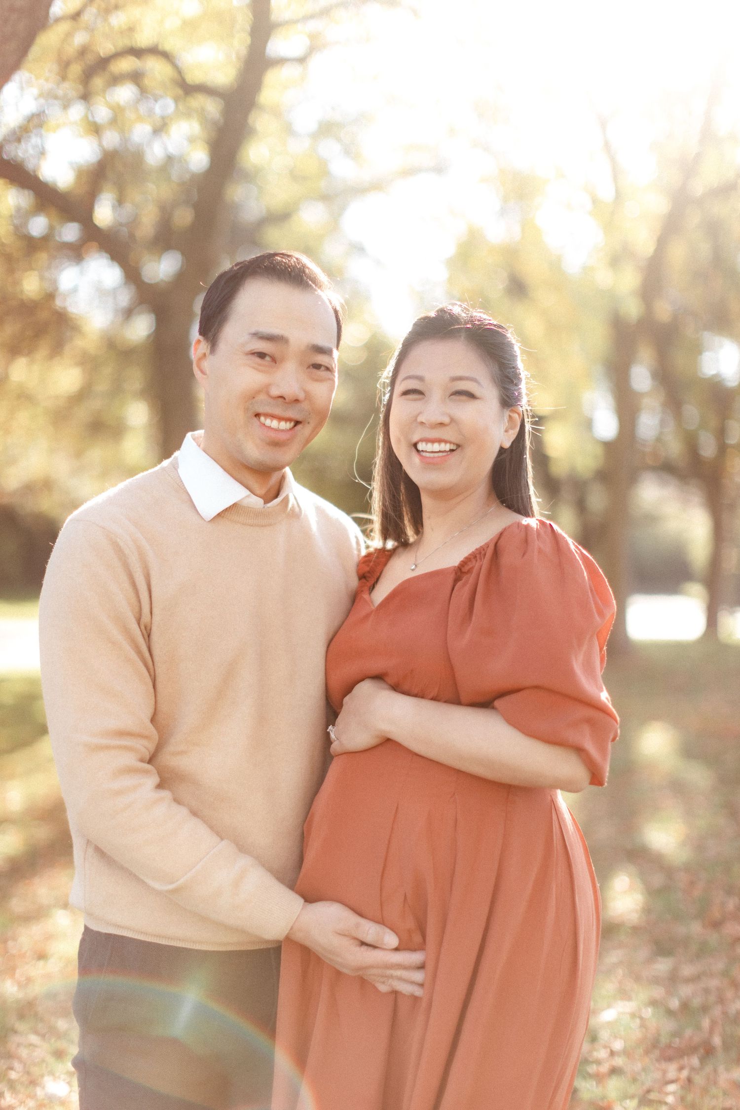Joyful couple laughing together during sunset maternity photography session in park.