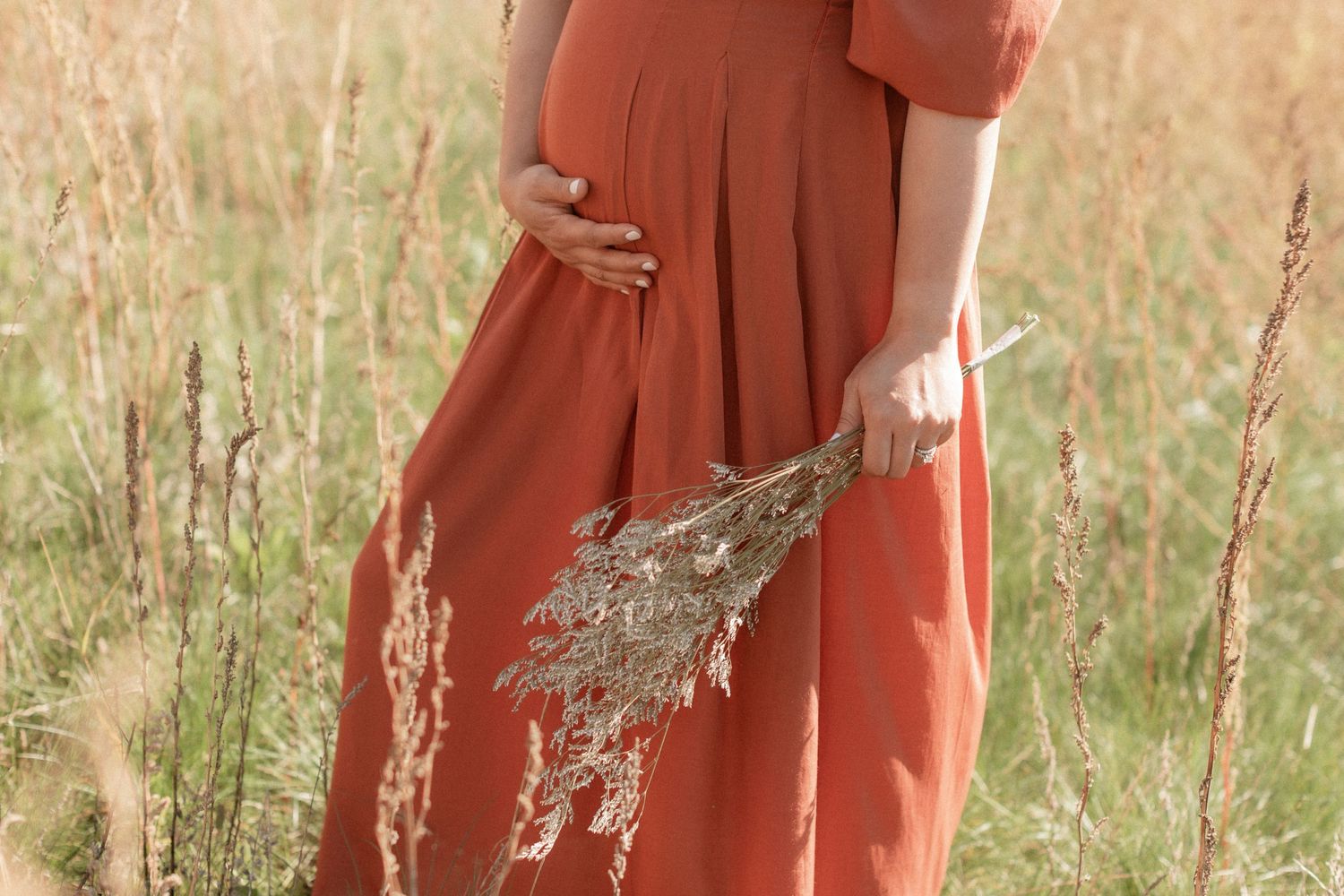Detail shot of rust-colored maternity dress against dried wheat stalks.