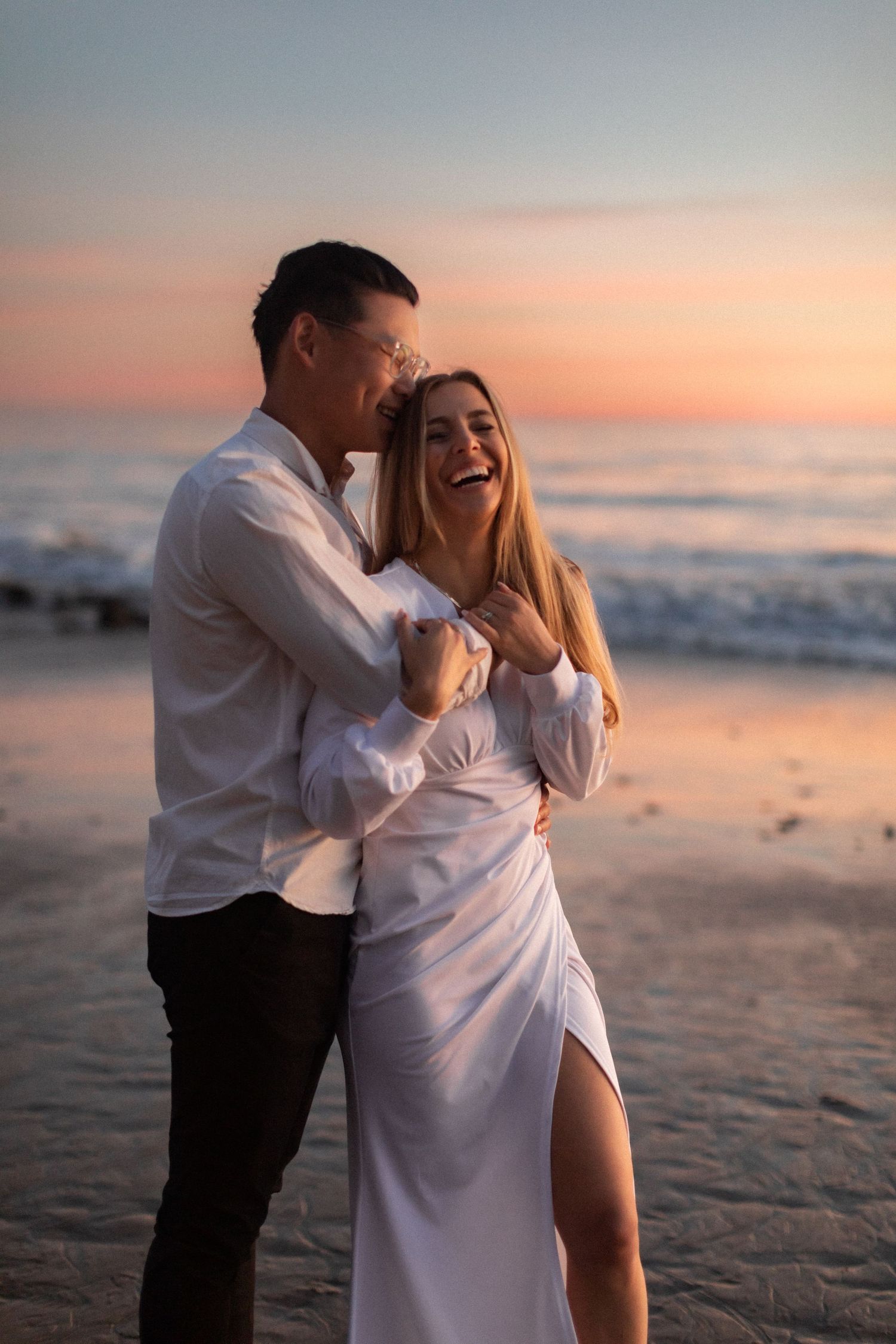 Romantic beach photoshoot of a couple laughing together at sunset on the sandy shore.