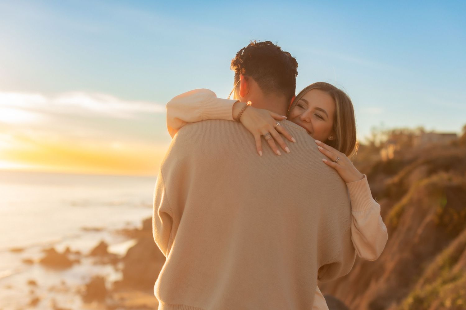 Intimate embrace shared between couple on scenic coastal overlook at sunset.