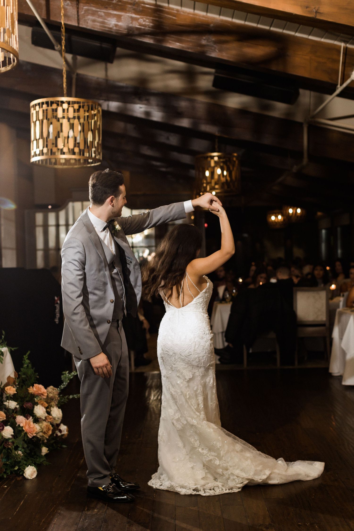 A couple dances in formal attire under geometric pendant lighting at their reception.