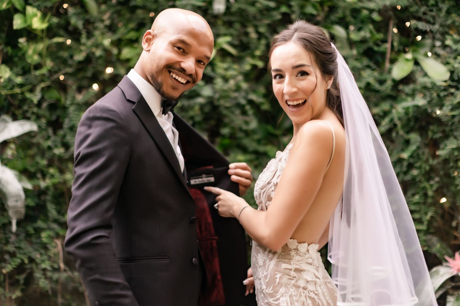 Joyful wedding couple smiling while exchanging rings in a lush garden setting.