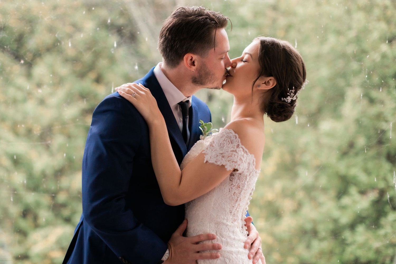 An intimate kiss between newlyweds surrounded by lush greenery and natural light.