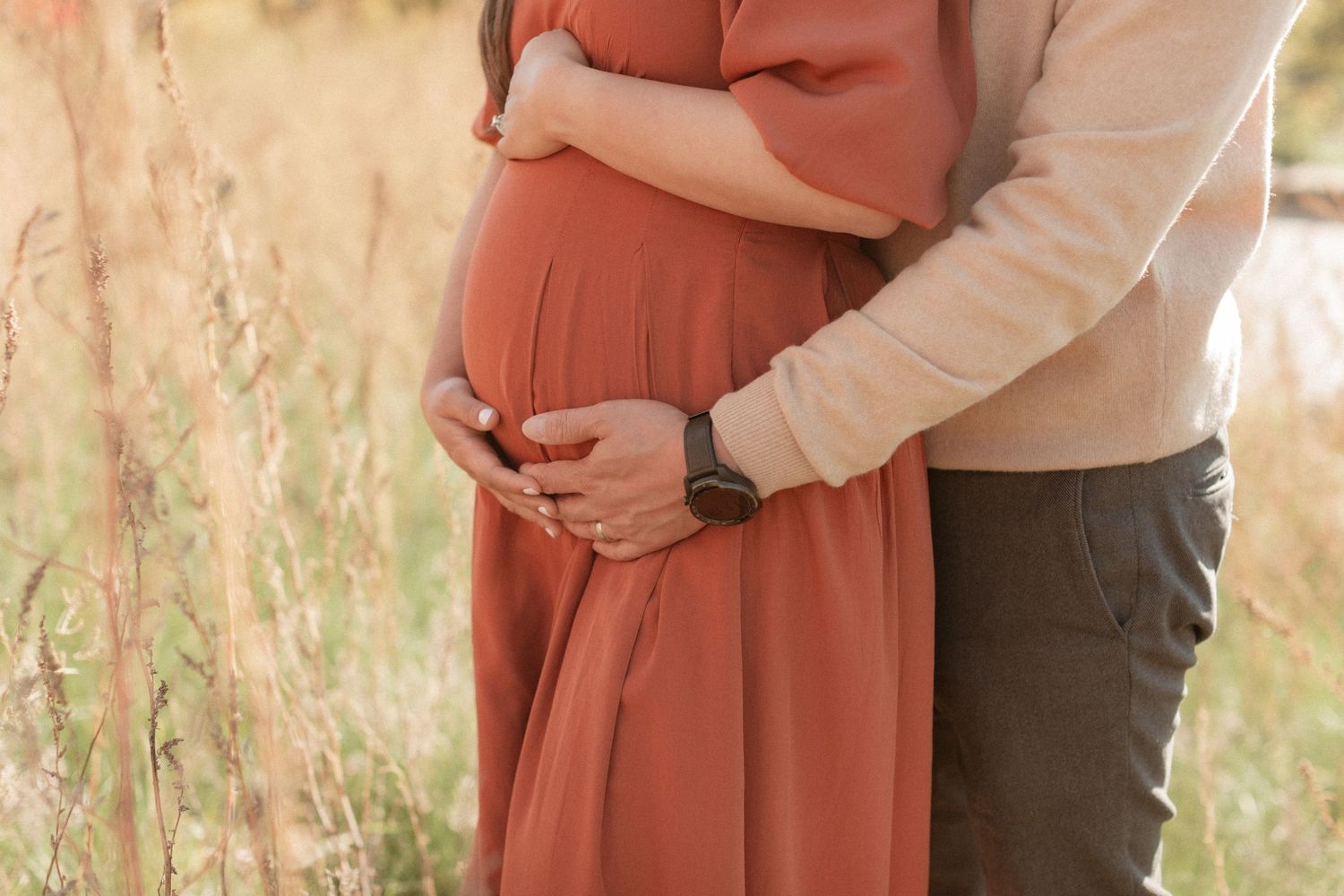 Close-up view of expecting couple embracing in a golden field at sunset.
