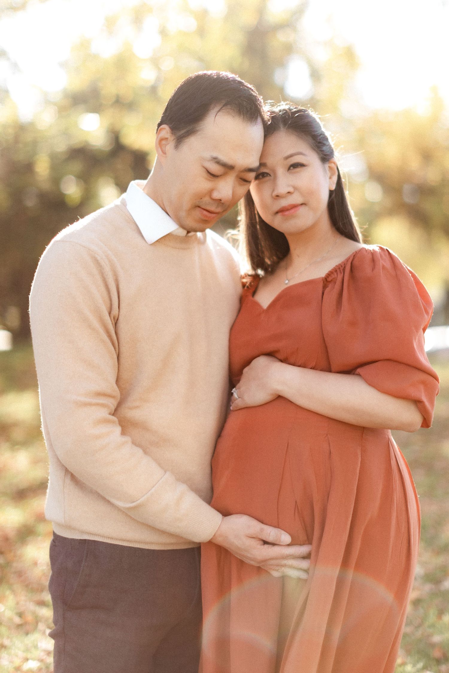 Intimate maternity portrait of couple sharing tender moment in warm autumn sunlight.