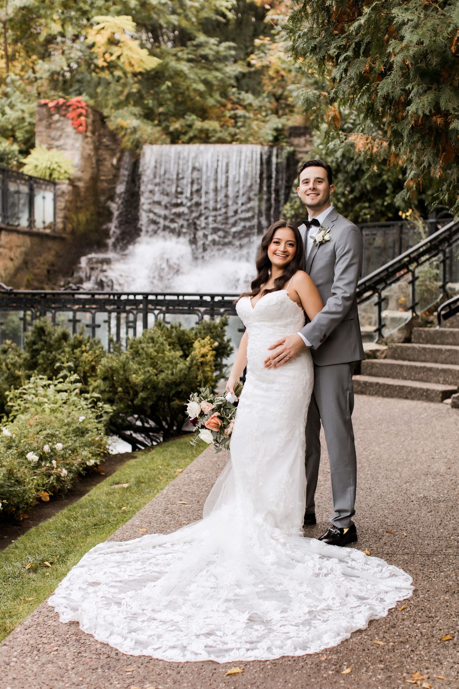 Full-length wedding portrait showcasing dramatic train against stone waterfall backdrop.