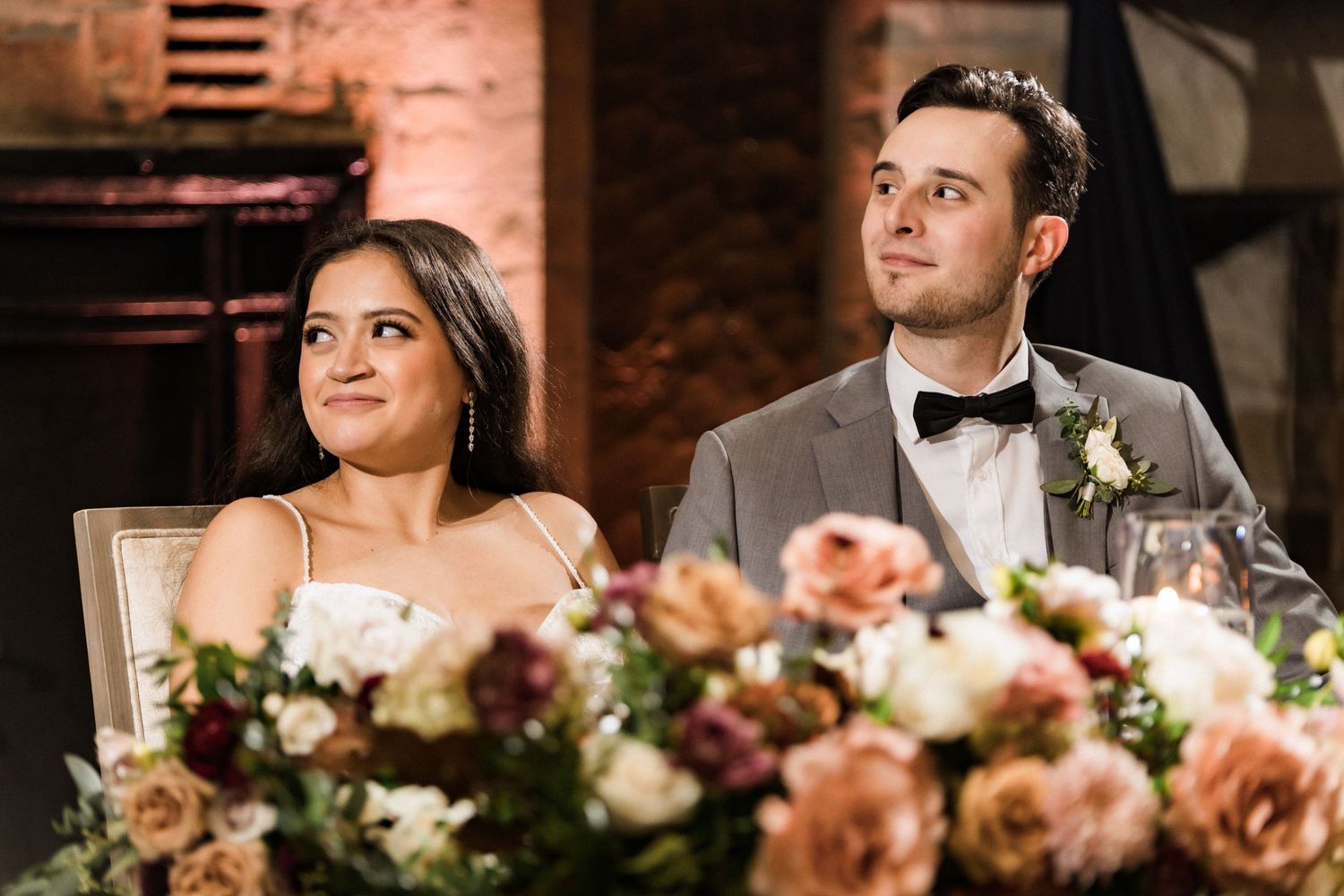A couple smiles at their wedding reception with peach floral centerpieces on the table.