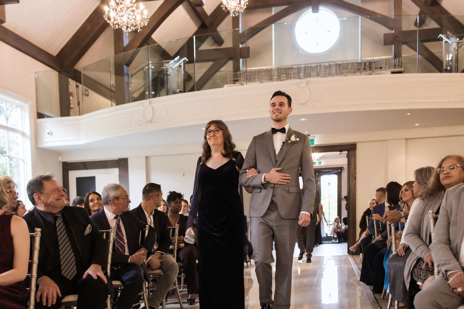 Wedding processional making their way down the aisle in an elegant chapel with rustic timber framing.