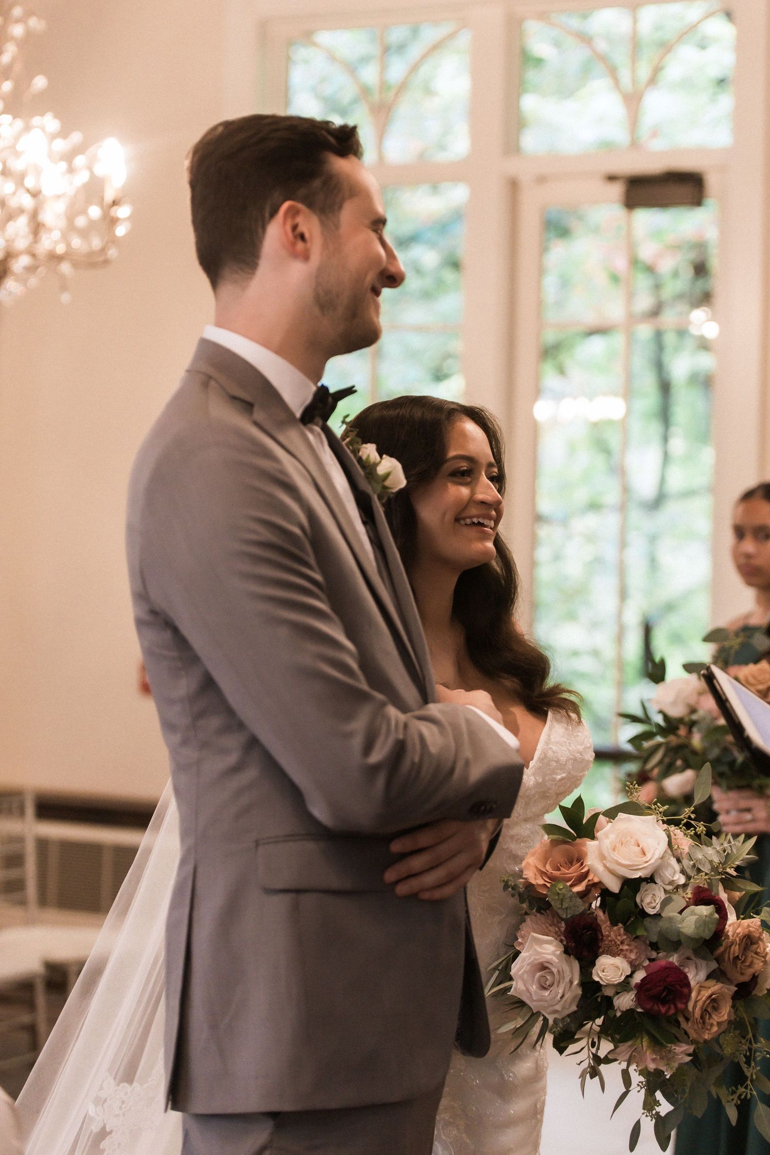 Intimate moment between newlyweds in a sun-filled room with crystal chandeliers and floral arrangements.