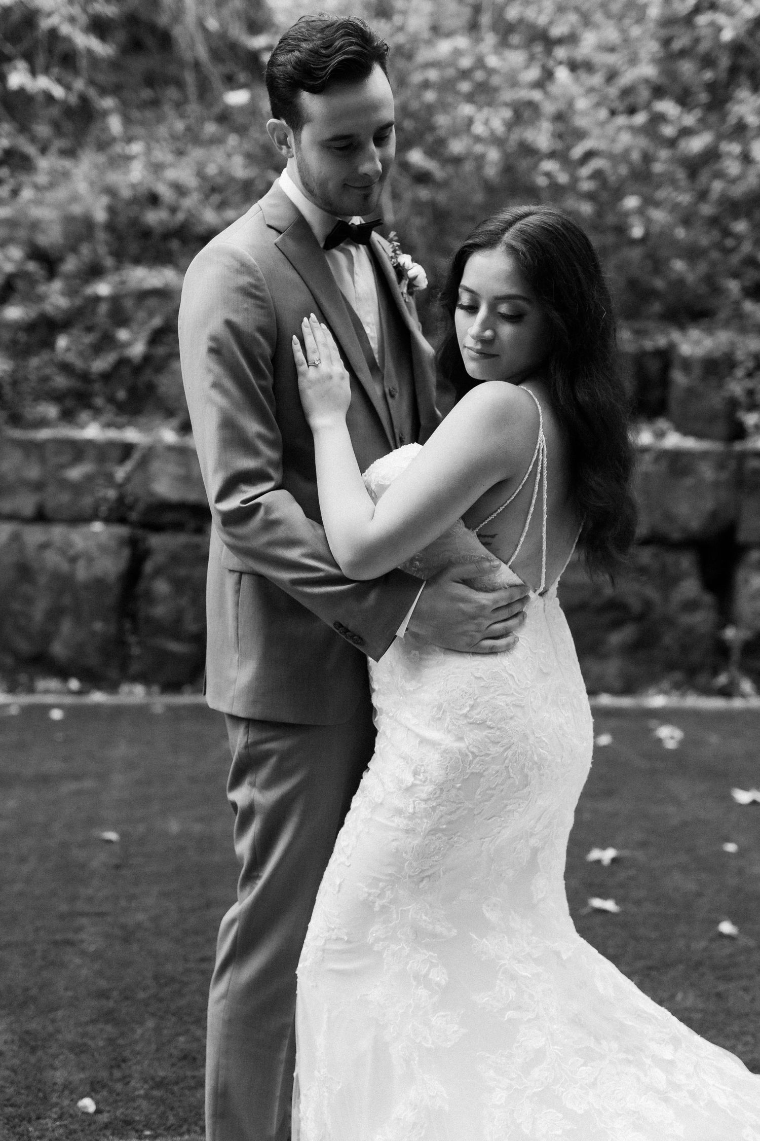 A romantic black and white wedding portrait of a couple embracing outdoors in formal attire.