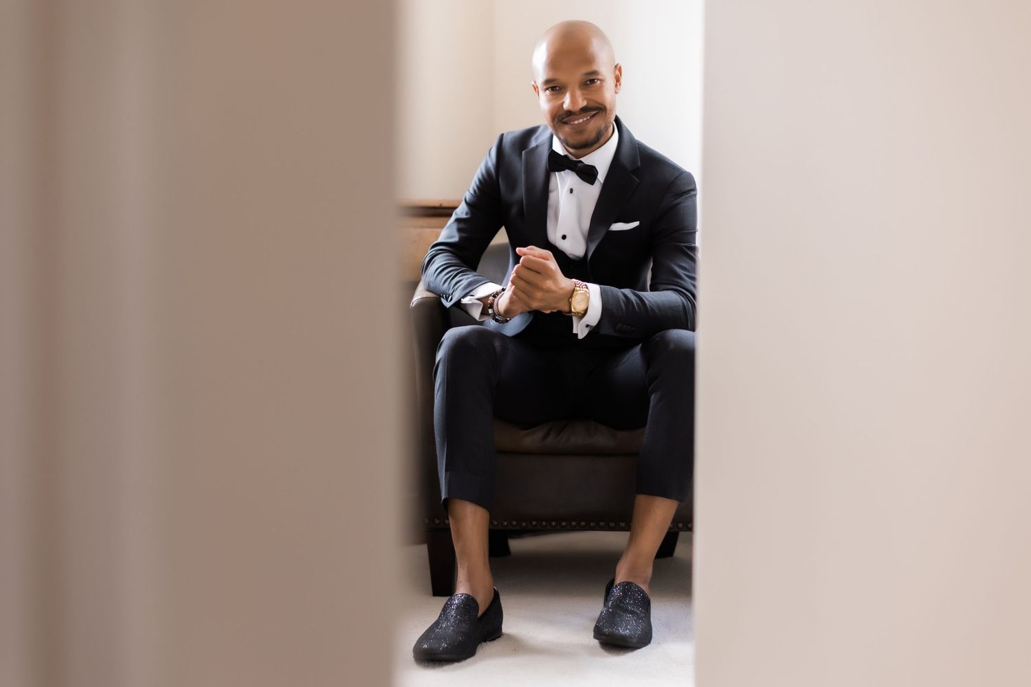Sophisticated portrait of person in formal attire sitting in brown leather armchair.