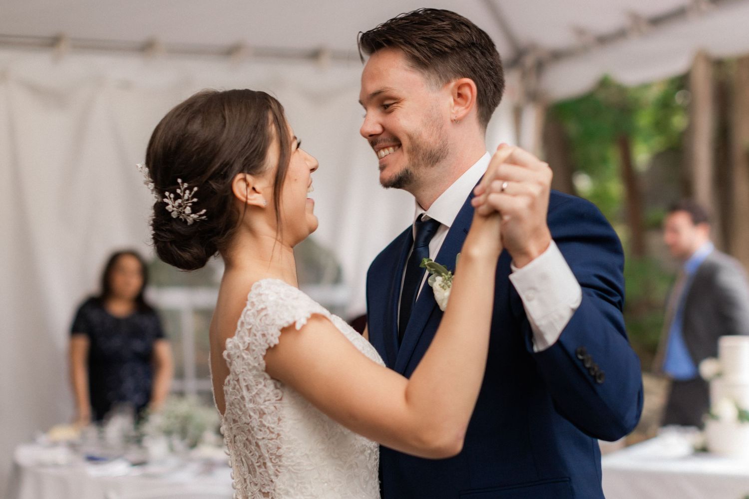 A couple shares an intimate dance moment under a white tent at their wedding reception.