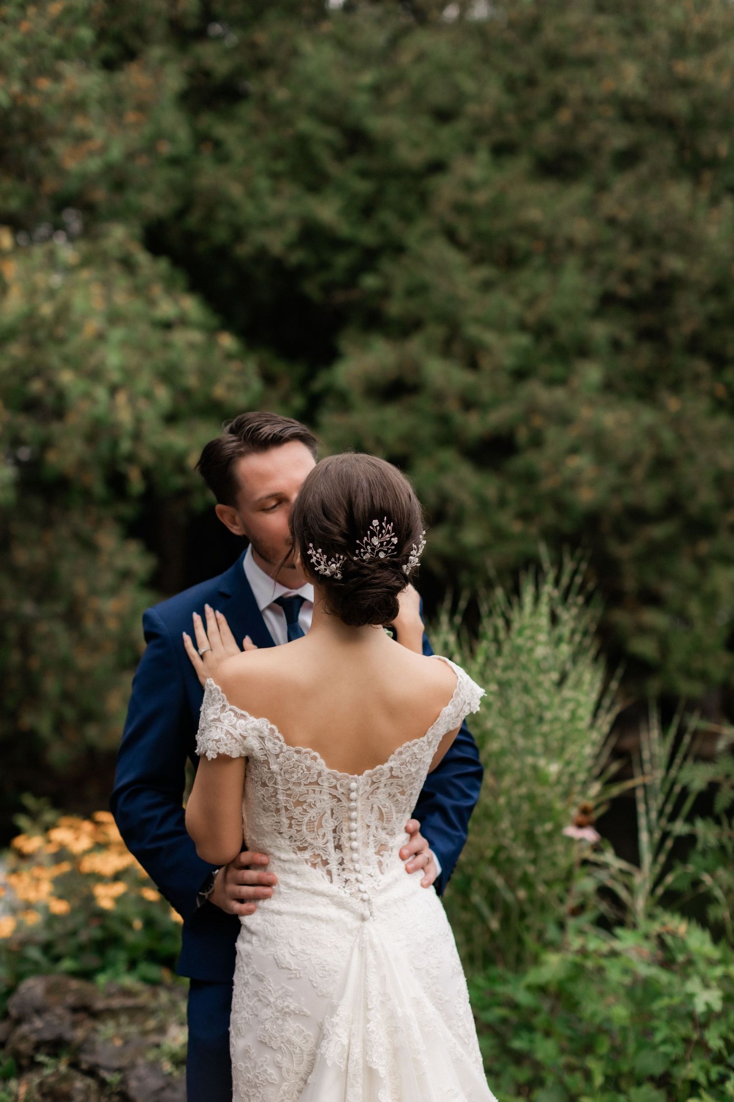 A couple in wedding attire share an intimate moment in a garden setting with greenery.
