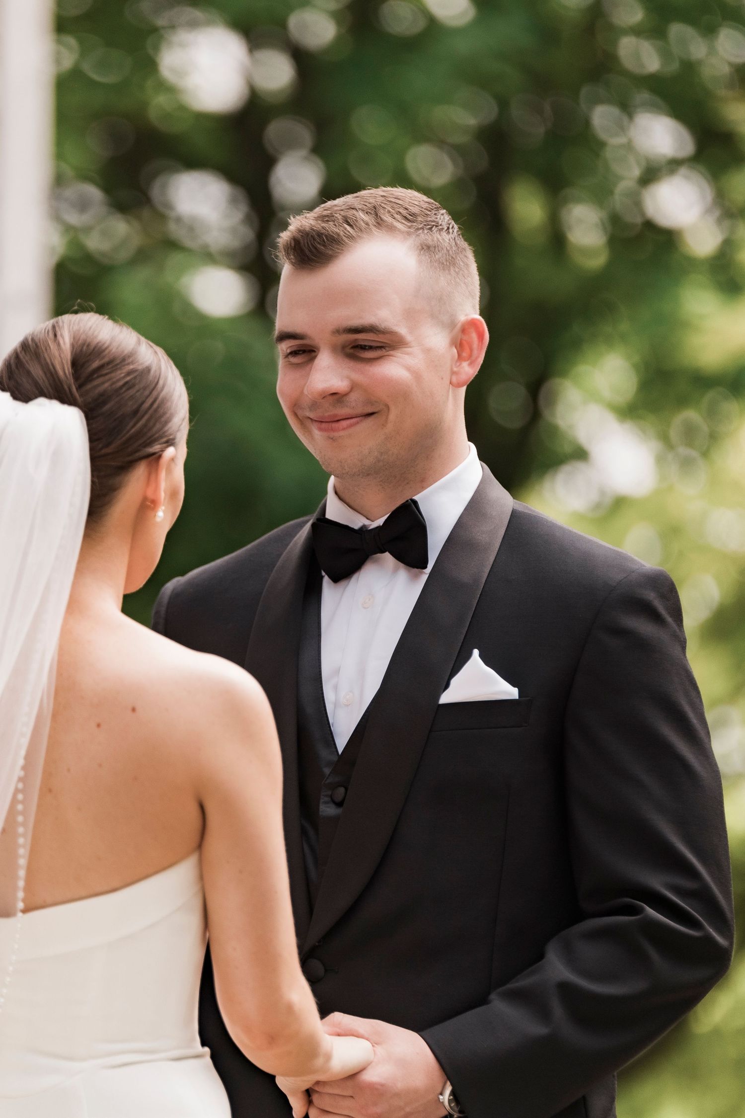 Wedding couple shares a tender moment outdoors with beautiful bokeh lighting in the background during their ceremony.