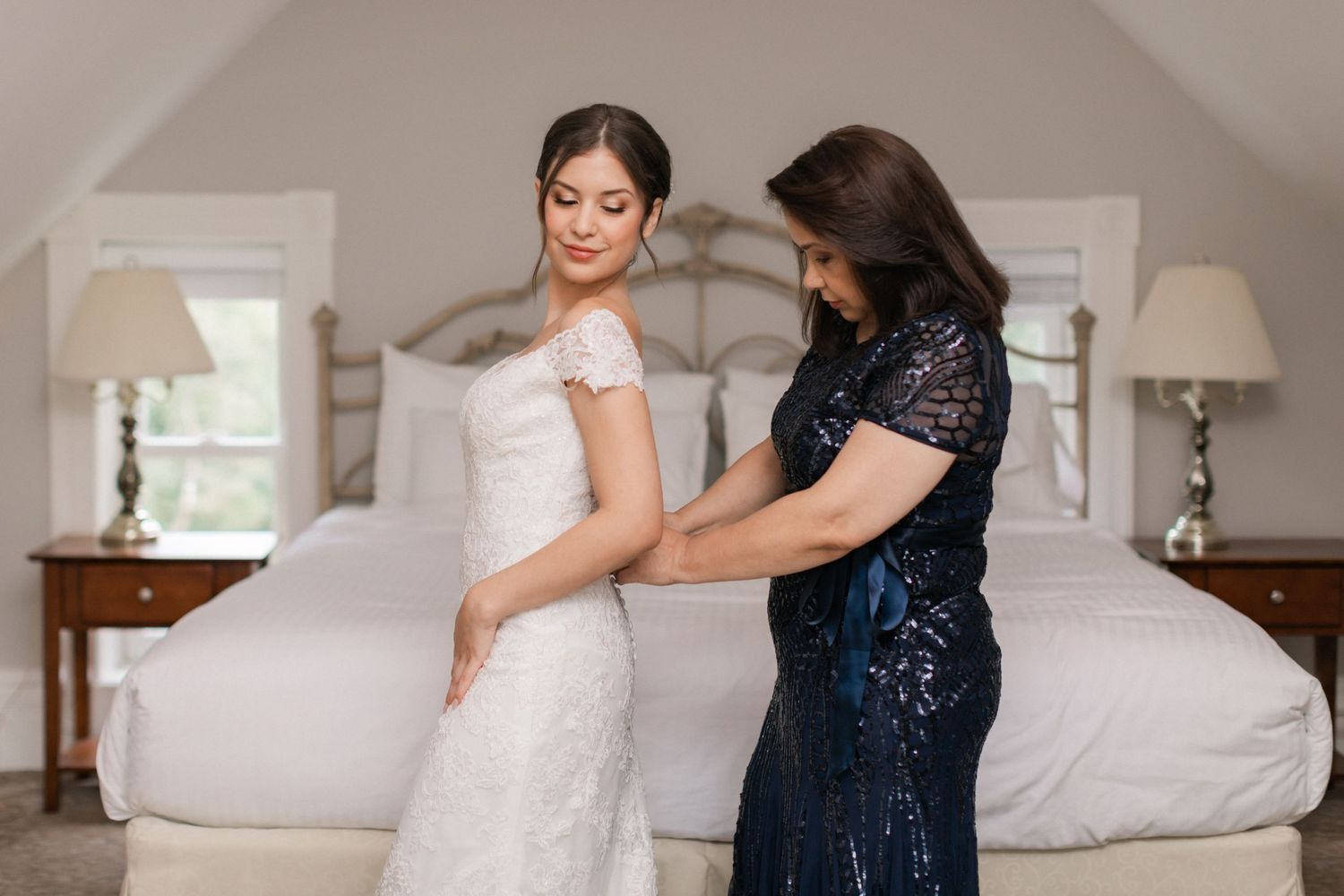 Bride in fitted lace gown with cap sleeves poses against ornate balcony railing.