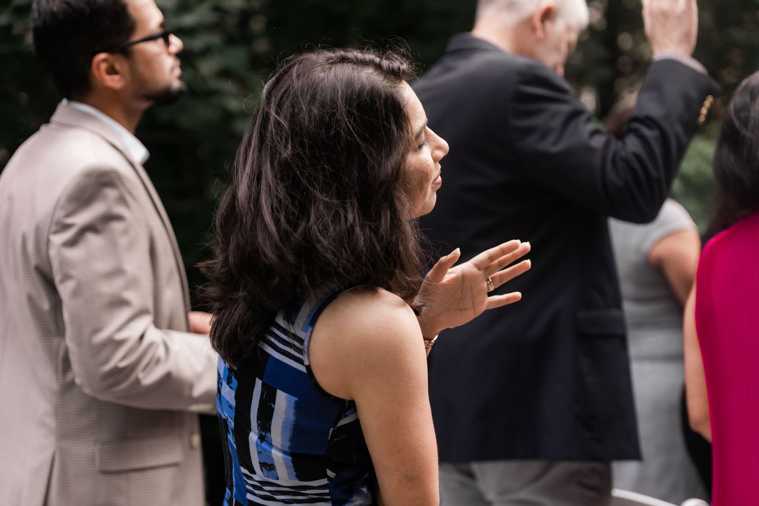 Wedding guests in formal attire clapping during an outdoor celebration.