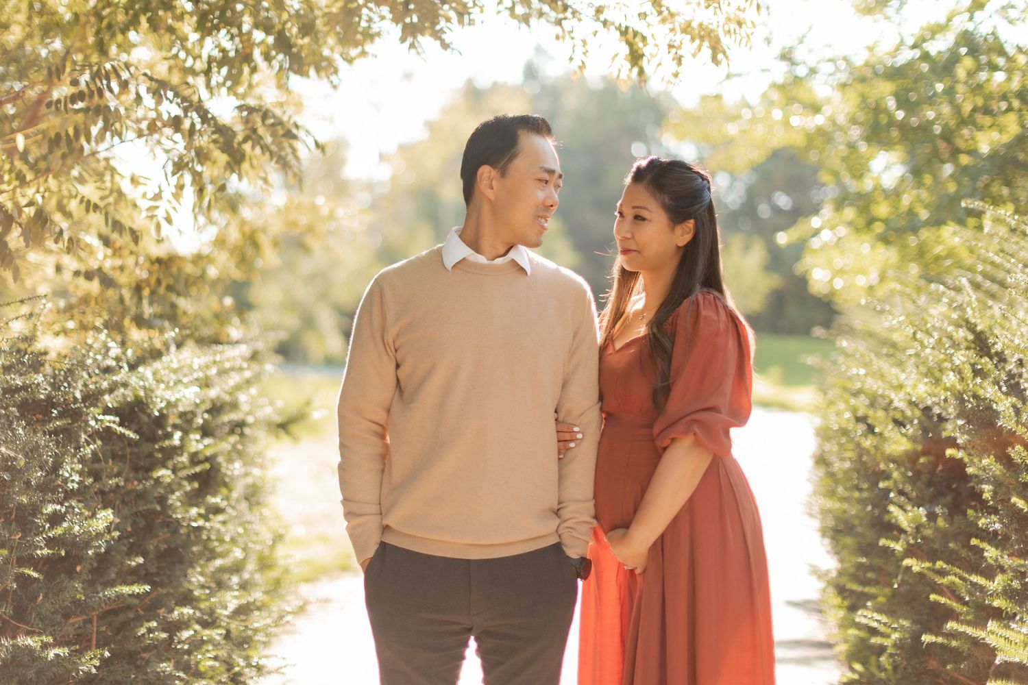 Couple shares loving glance during outdoor maternity session with golden backlight.